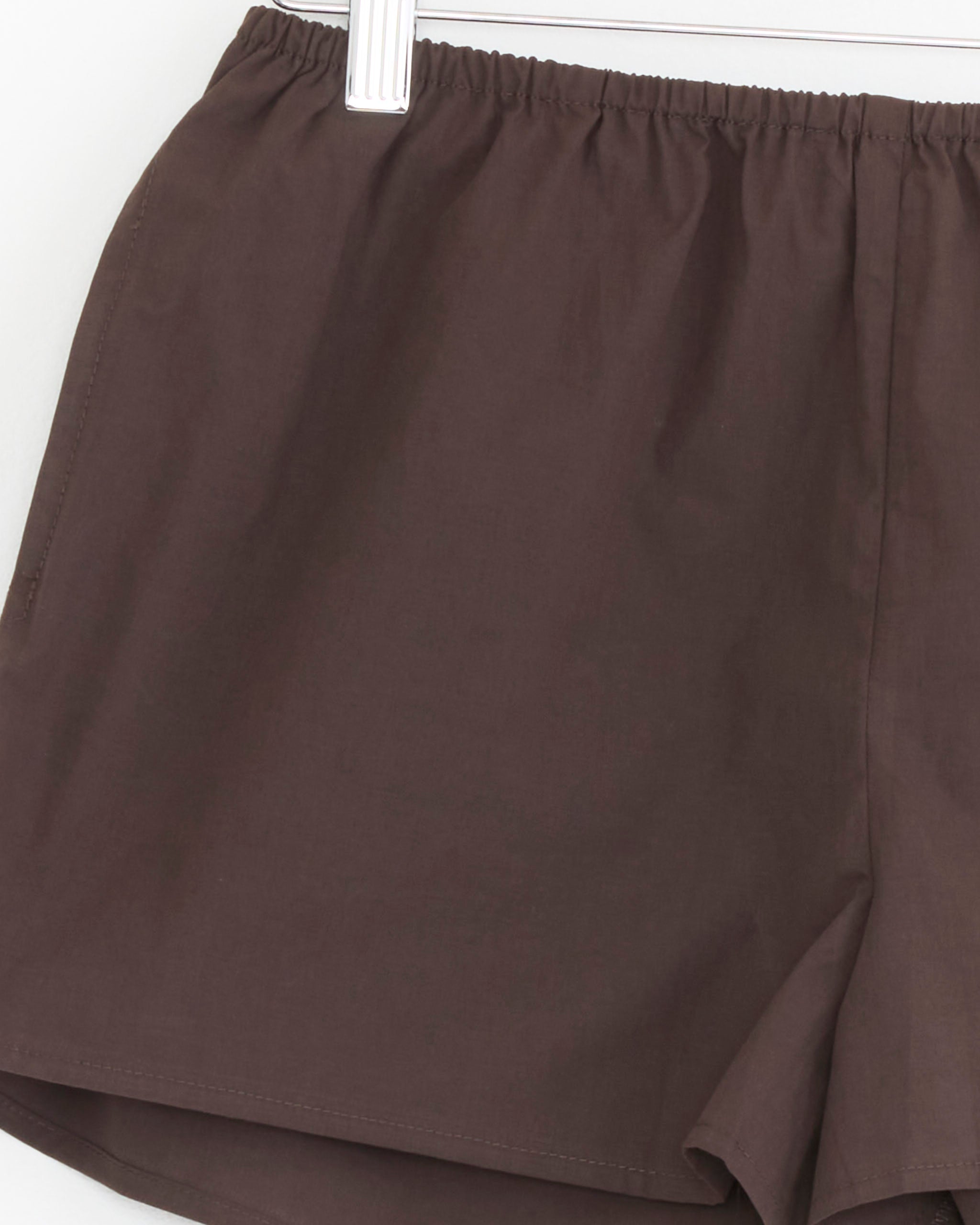A close-up of the Bind Set in Sepia by Deiji Studios—a brown cami and boxer short set with an elastic waistband—hanging on a white hanger against a white background.