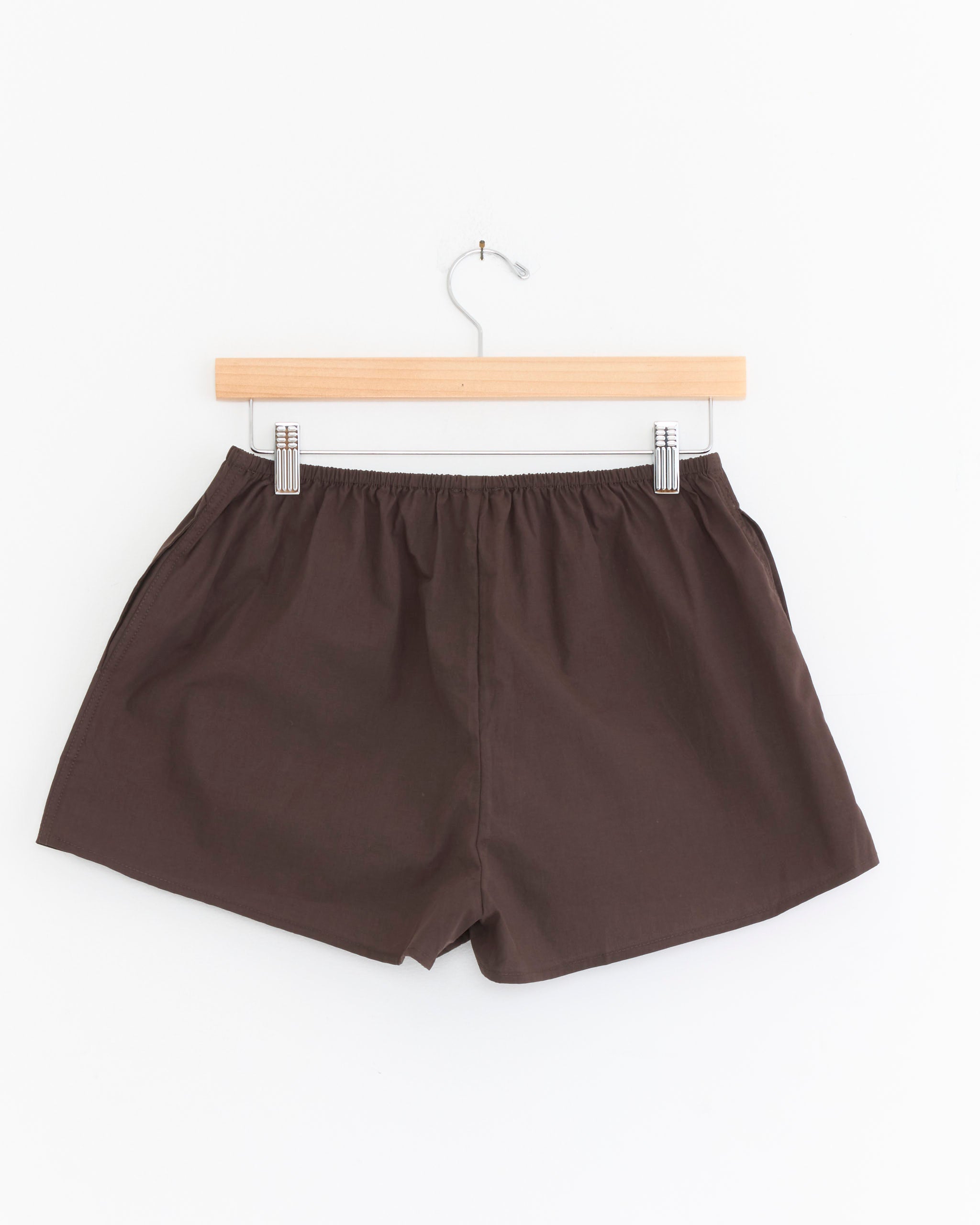 The Bind Set in Sepia by Deiji Studios features dark brown boxer shorts with an elastic waistband, displayed on a wooden hanger against a white background.