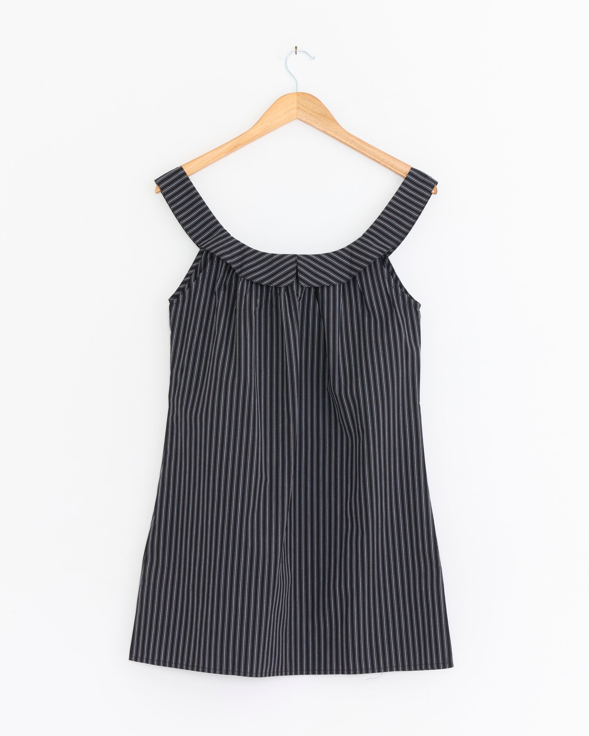 The Deiji Studios Round Neck Dress in Mono Stripe, featuring thin vertical white stripes on black, hangs on a wooden hanger against a plain white background.