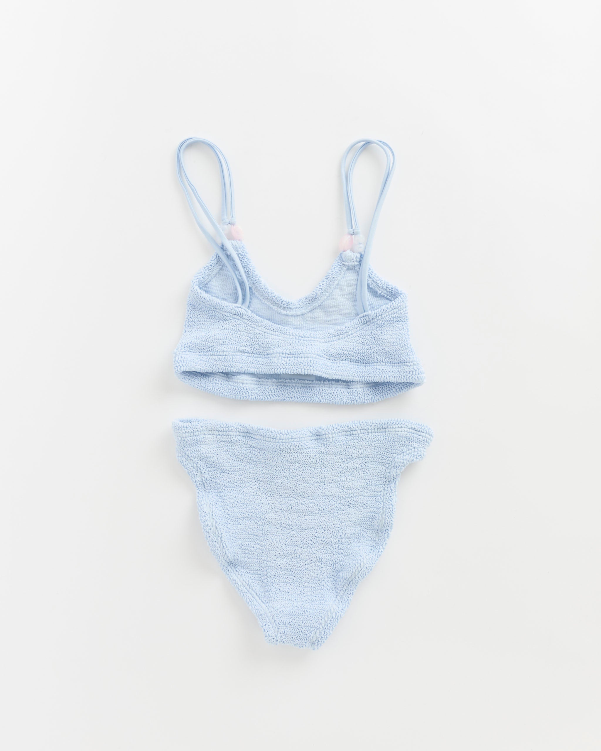 The Cassie Beaded Bikini in Metallic Ice Blue by Hunza G, featuring adjustable spaghetti straps and high-waisted bottoms, is displayed laid flat on a white background.