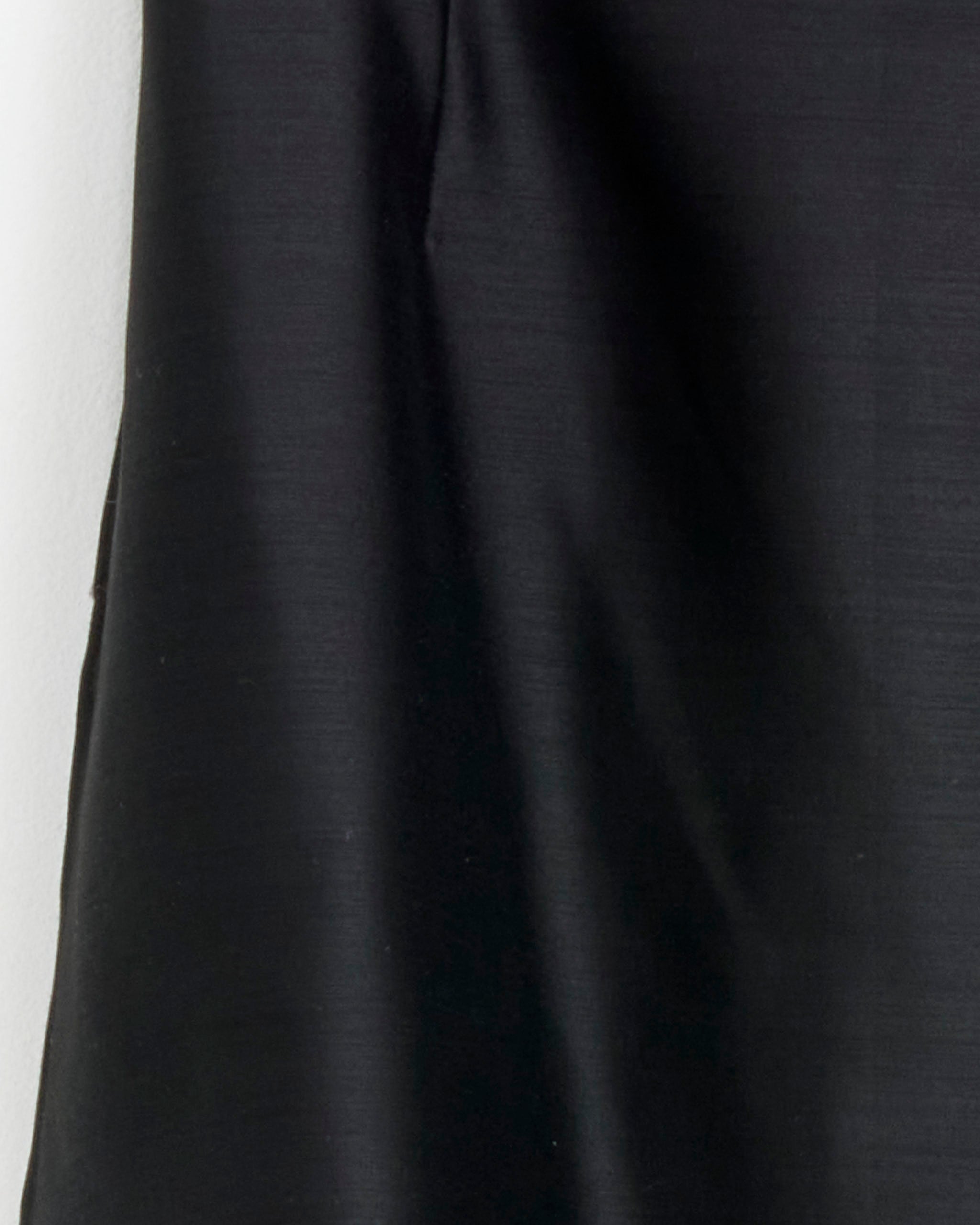 Close-up of the Clare Skirt in Black by Chelsea Mak, showing part of the sleek, subtly shiny fabric with gentle folds against a light background.