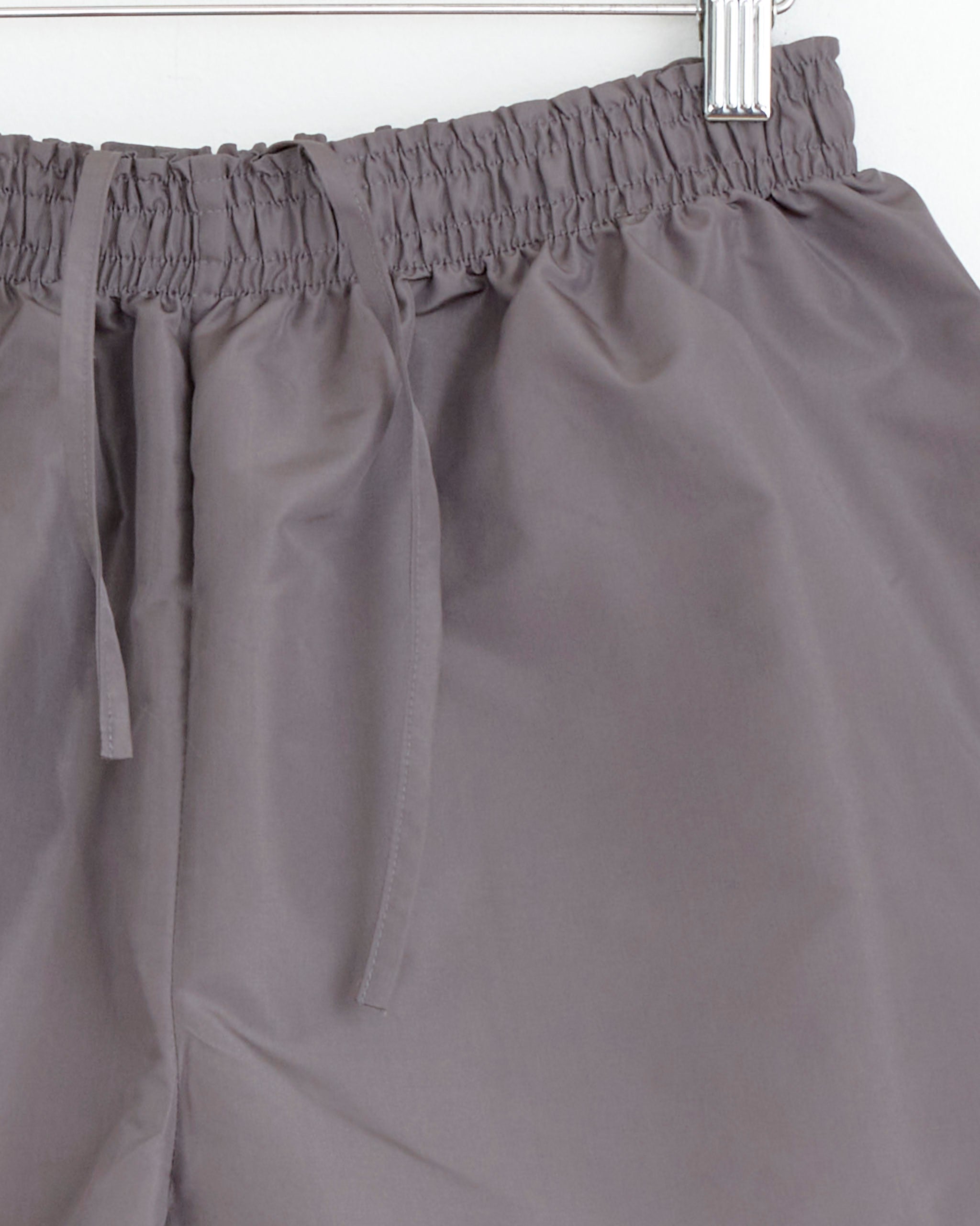 Close-up of the waistband of Chelsea Mak’s Asa Short in Metal, featuring a gray drawstring, hanging on a hanger against a white background.
