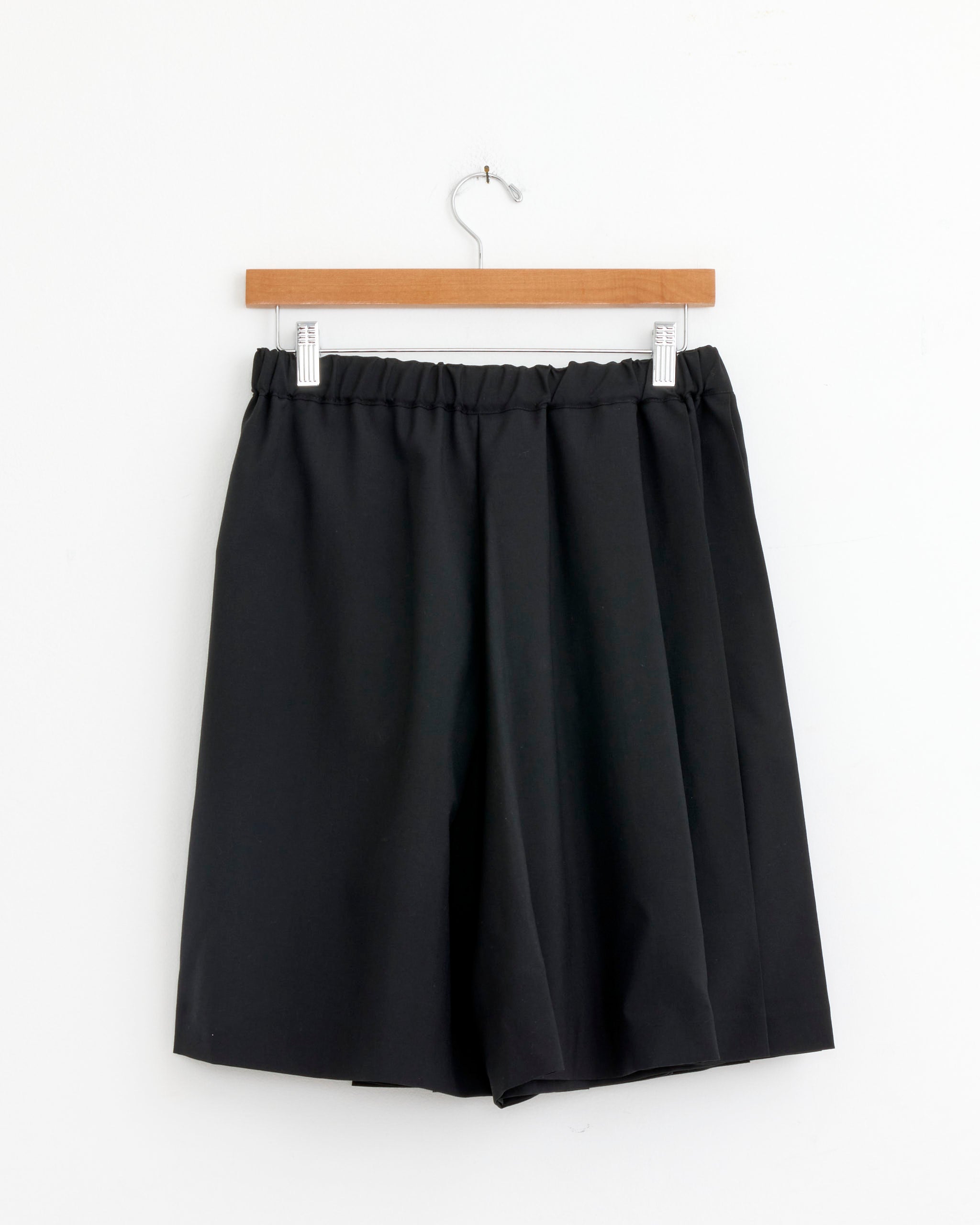 The Comme Des Garçons Girl P008 Skirt in black, made of 100% wool with an elastic waistband, hangs on a wooden hanger against a plain white background. Available at Mohawk General Store.