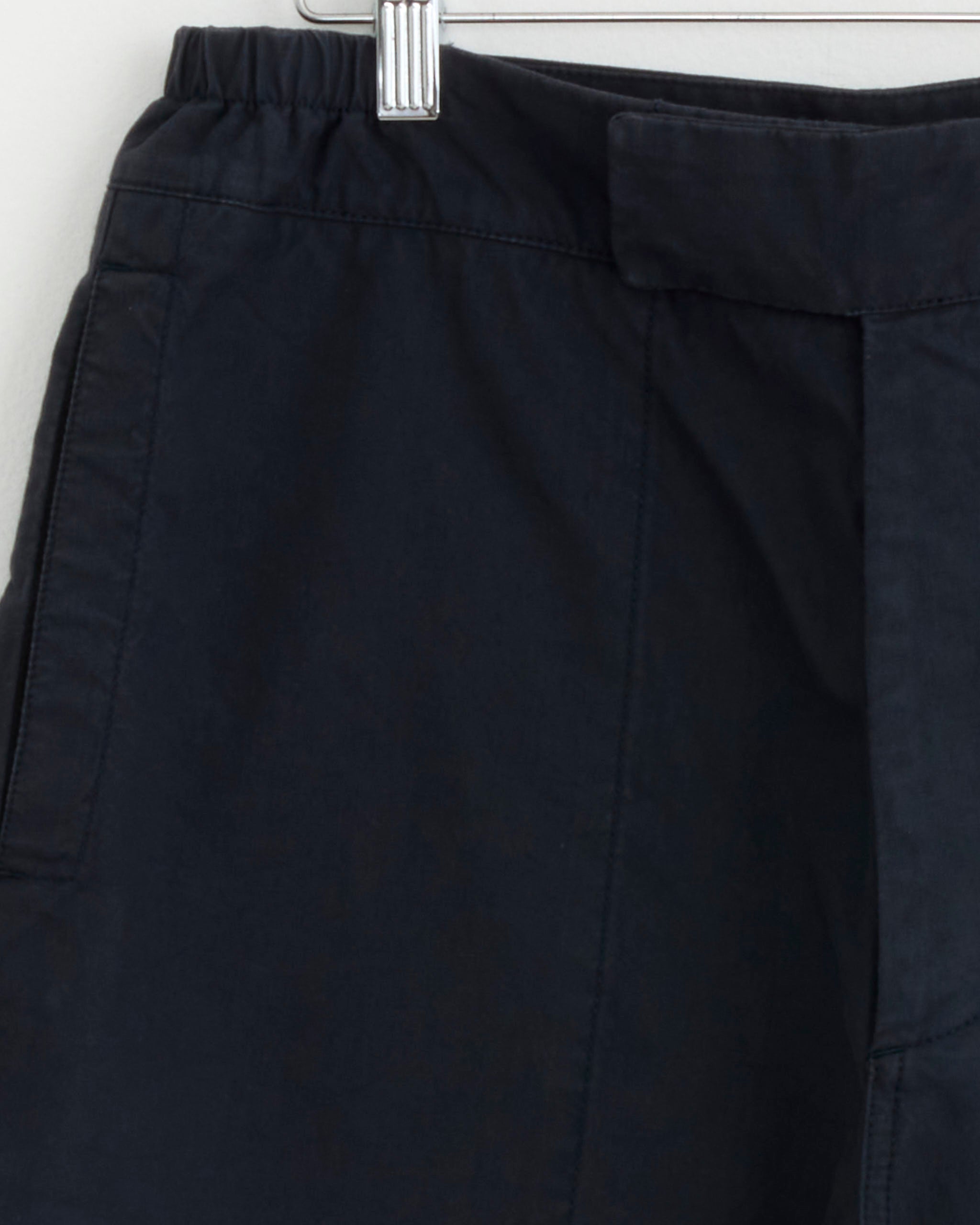 Close-up of the Gym Short in Ink by MHL by Margaret Howell, hanging on a hanger, highlighting the waistband, belt loop, and upper leg with visible stitching on dark navy ripstop cotton.