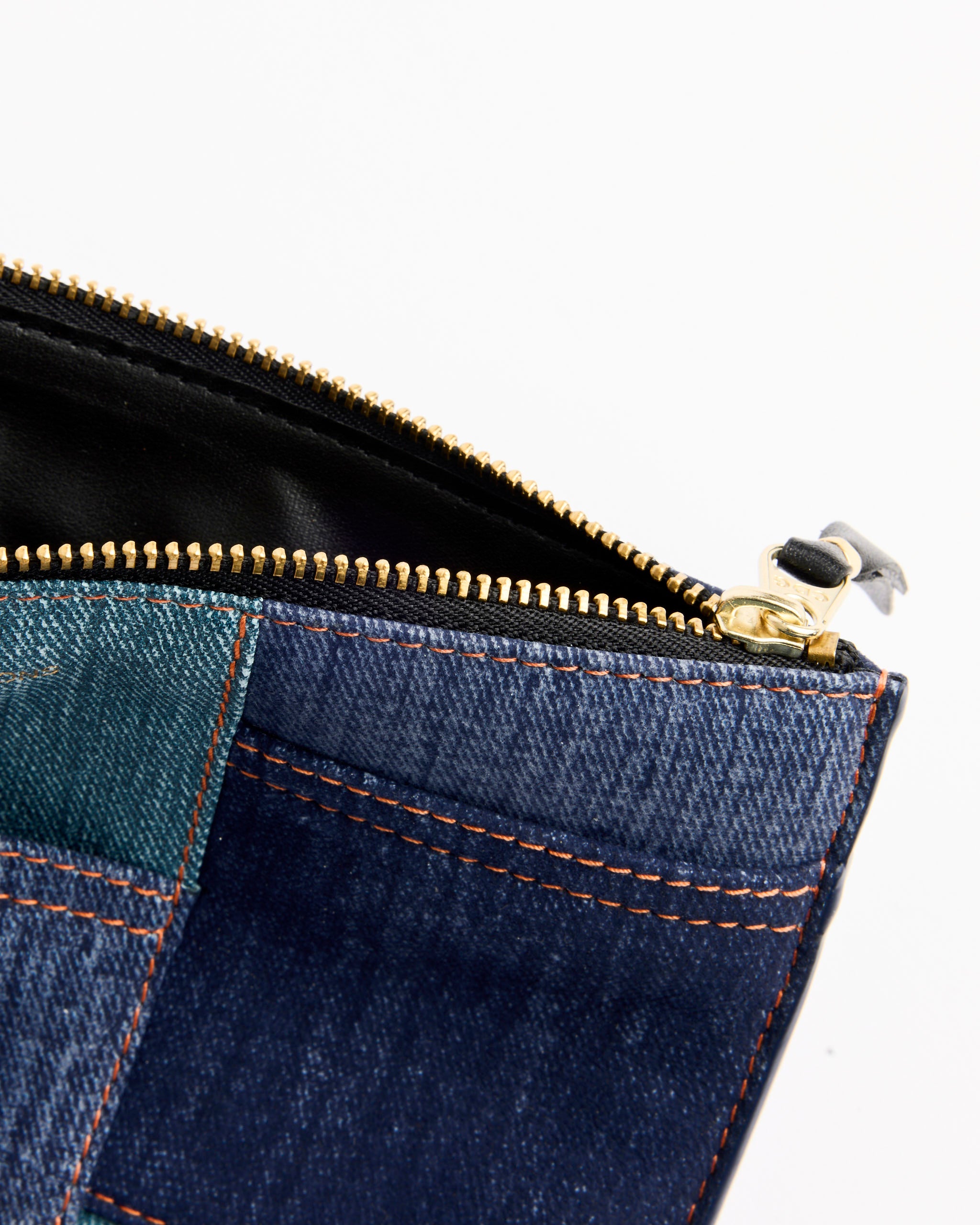 Close-up of the Denim Pocket Wallet in Blue by Comme des Garçons Wallet, crafted from patchwork denim with orange stitching, a gold zipper partly opened to show its black interior, set against a white background.
