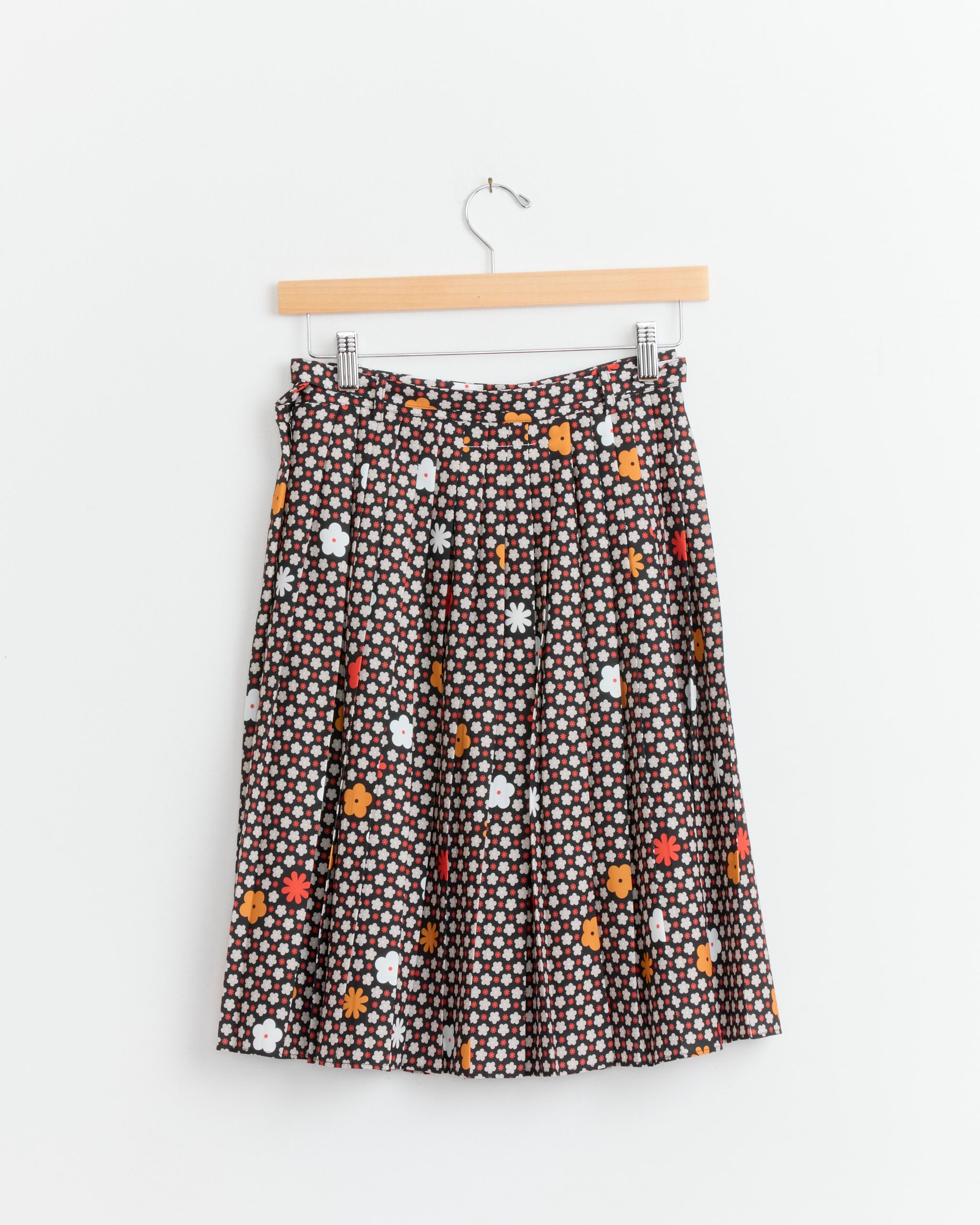 The MM6 Maison Margiela S62MA0102 Skirt in Black/Red is displayed on a wooden hanger against a plain white wall, showcasing its stylish knee-length pleated design.