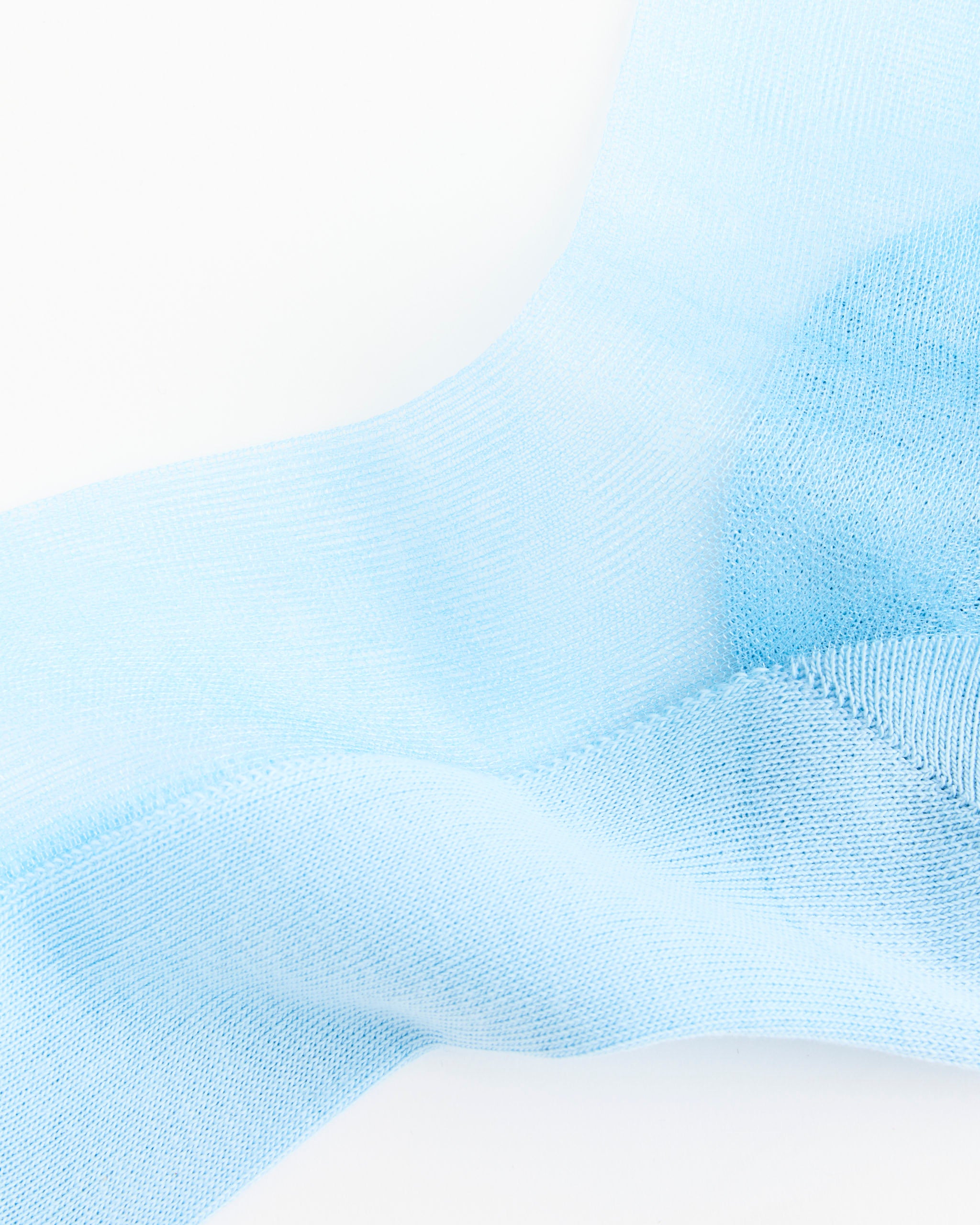 A close-up of the MM6 Maison Margiela Bootleg Knee High Socks in Shirt Blue, featuring light blue, semi-transparent knitted fabric with soft folds and flowing shapes set against a white background.