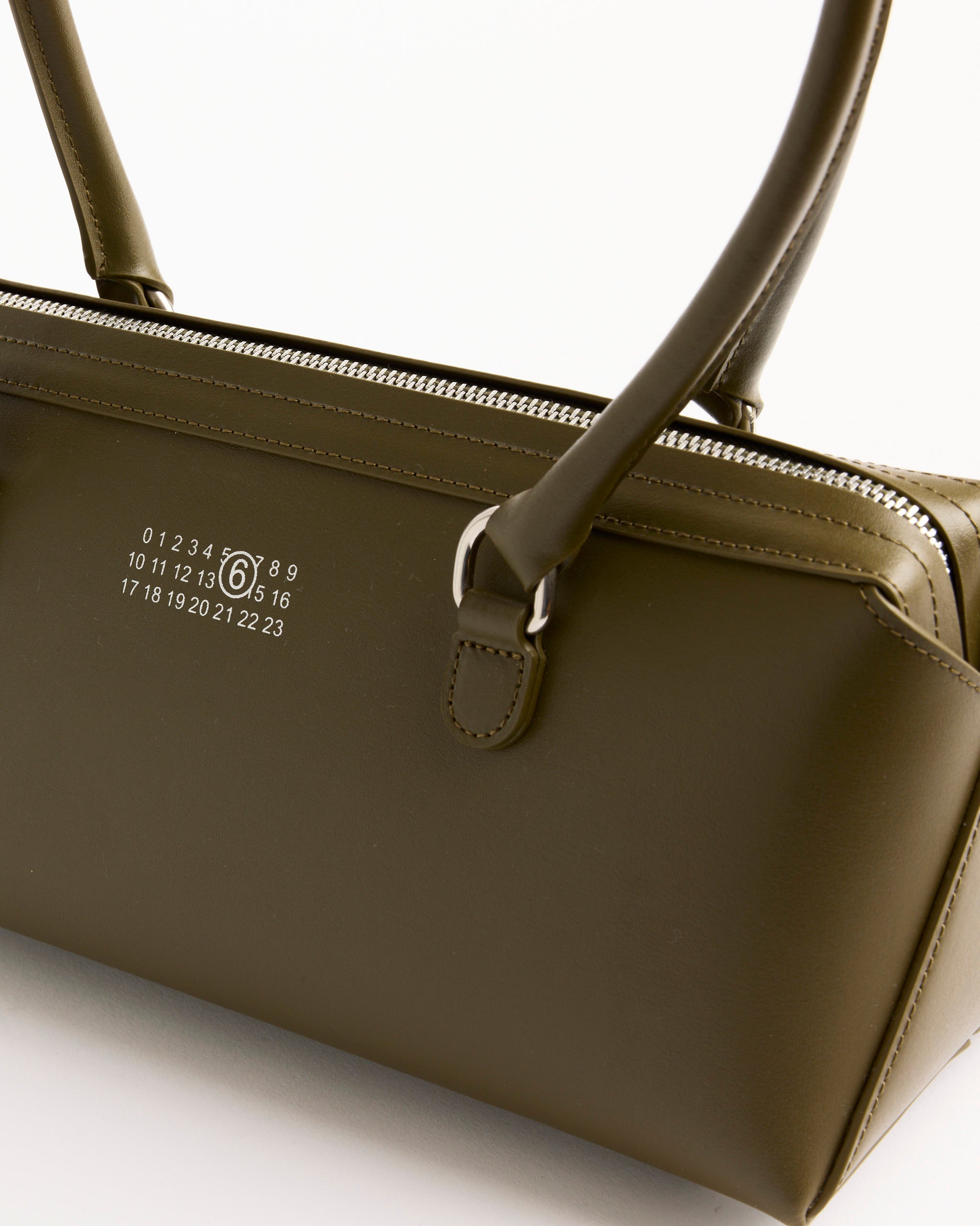 A close-up of the New Bauletto J Medium Bag in khaki by MM6 Maison Margiela, featuring silver zippers, dual handles, and a white numeric logo (0–23) on the side for a modern minimalist look.