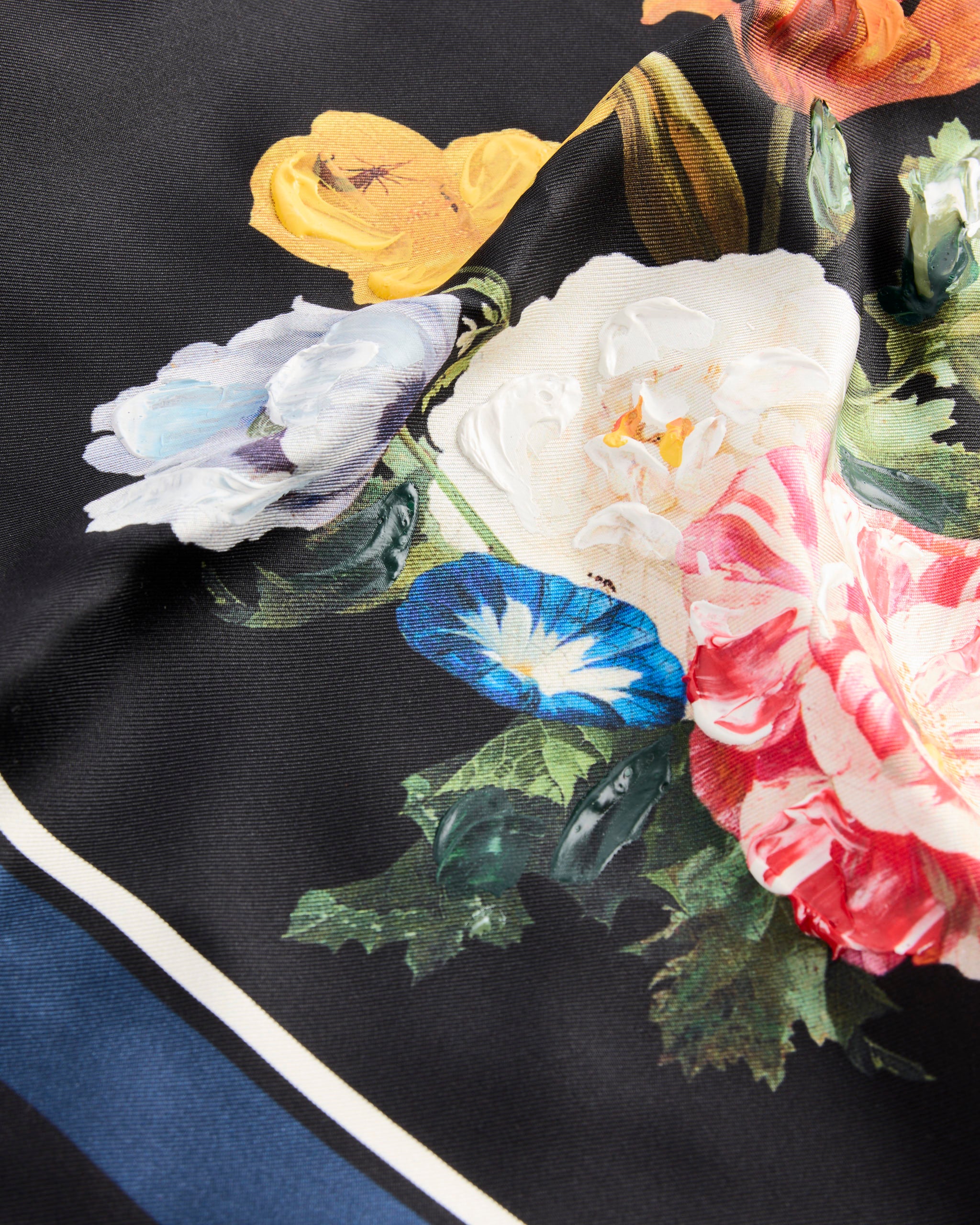 A close-up of Maison Margiela's Silk Scarf in Black, crafted from silk twill and featuring vibrant red, yellow, white, blue, and light purple floralprints with green leaves, framed by crisp white and blue stripes.