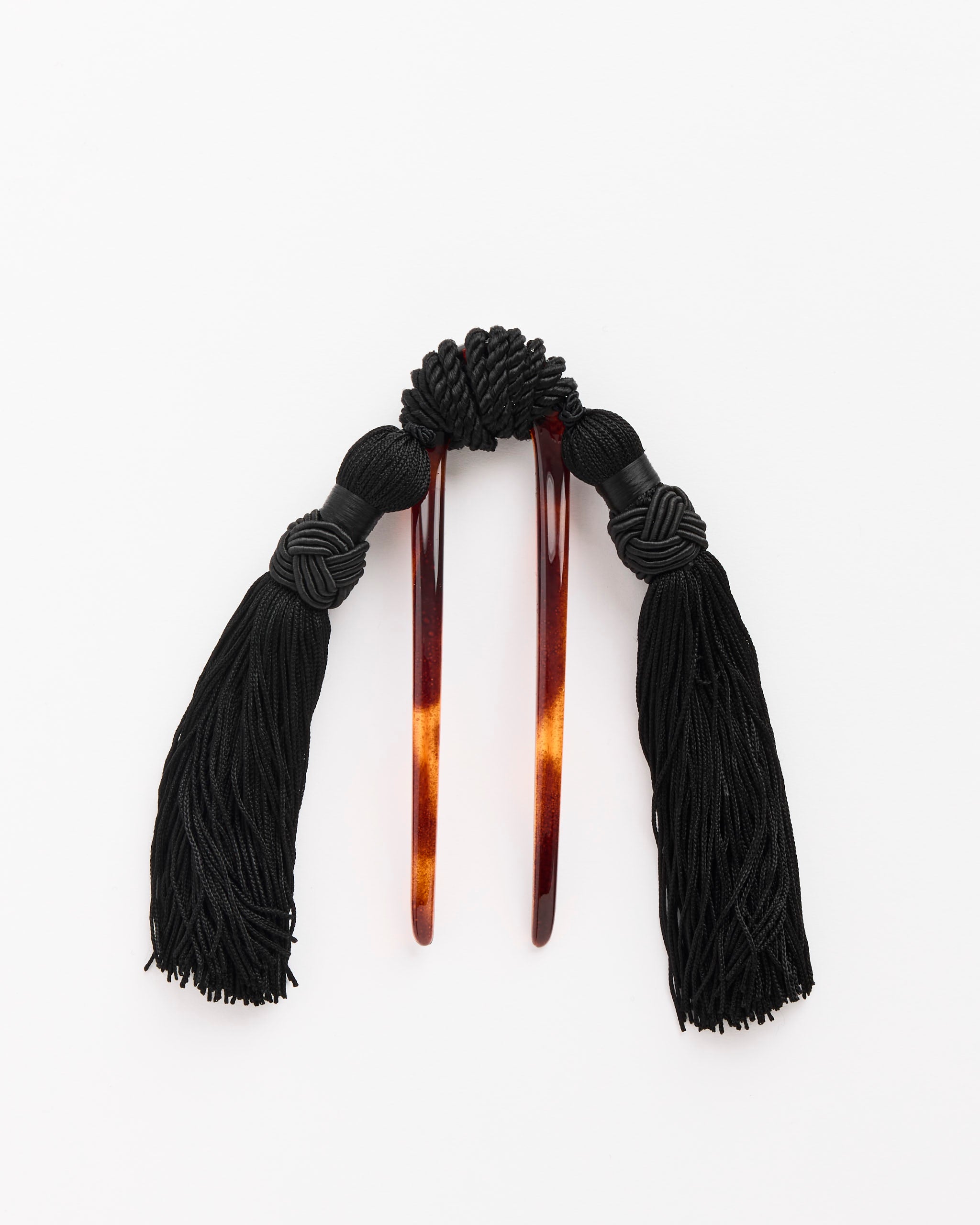 The Mosquito Vega Hair Comb with Silk Tassels features two brown tortoiseshell-style prongs, each with intricate black cord knots and thick black tassels. For fit or sizing details, contact our online chat support. Shown on a white background.