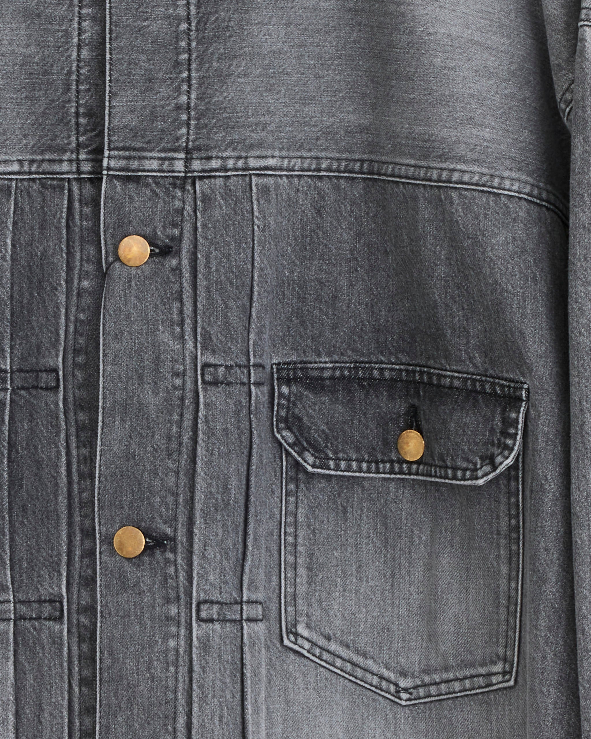 Close-up of the Auralee Dyed Duck Blouson in Faded Black, an organic cotton jacket with gold buttons and a right-side breast pocket. Visible stitching and light wear give it vintage character.