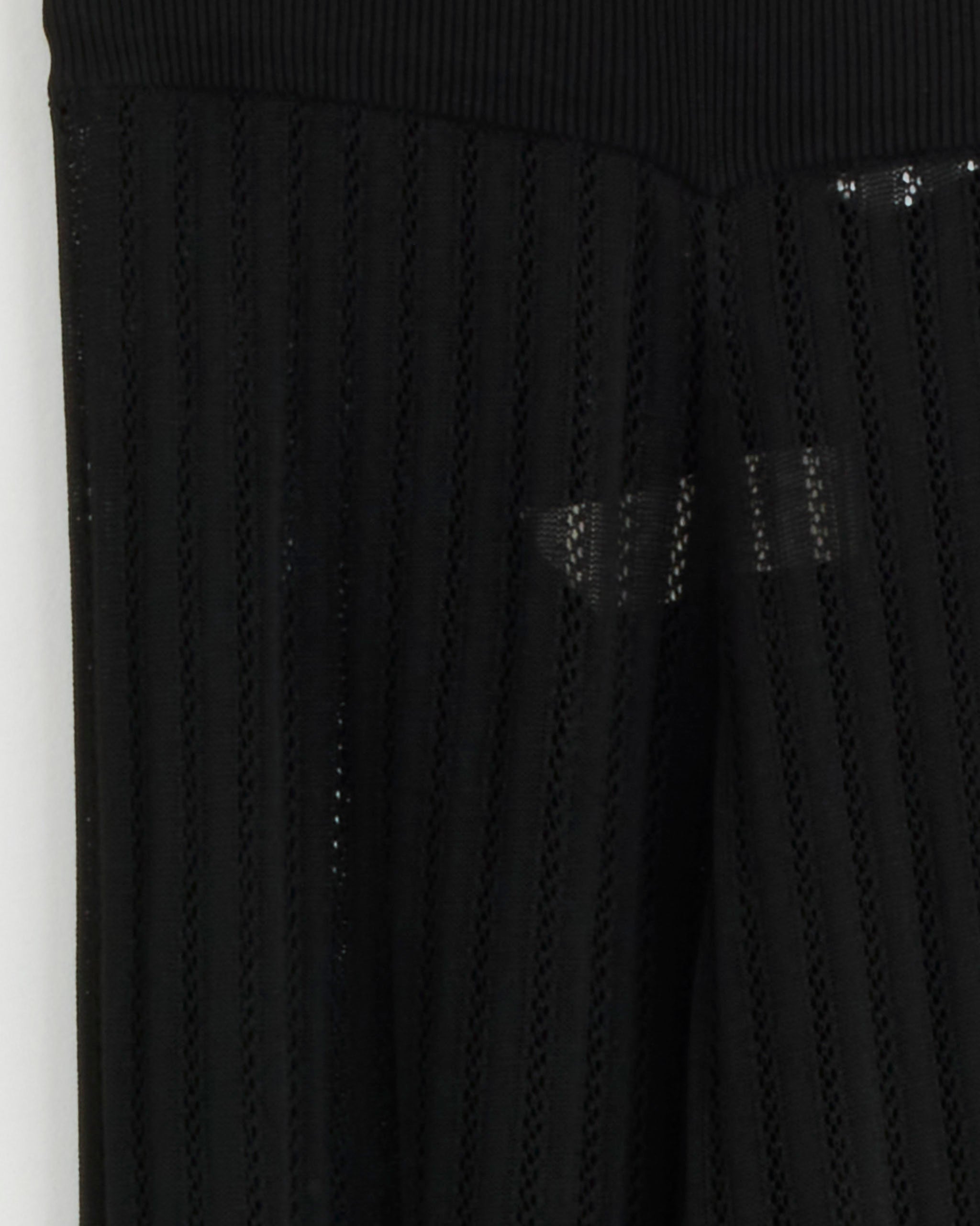 Close-up of CORDERA's Lace Knit Pant in Black, featuring ribbed semi-sheer fabric with vertical textured lines and a solid waistband. The slightly see-through material reveals a faint background.
