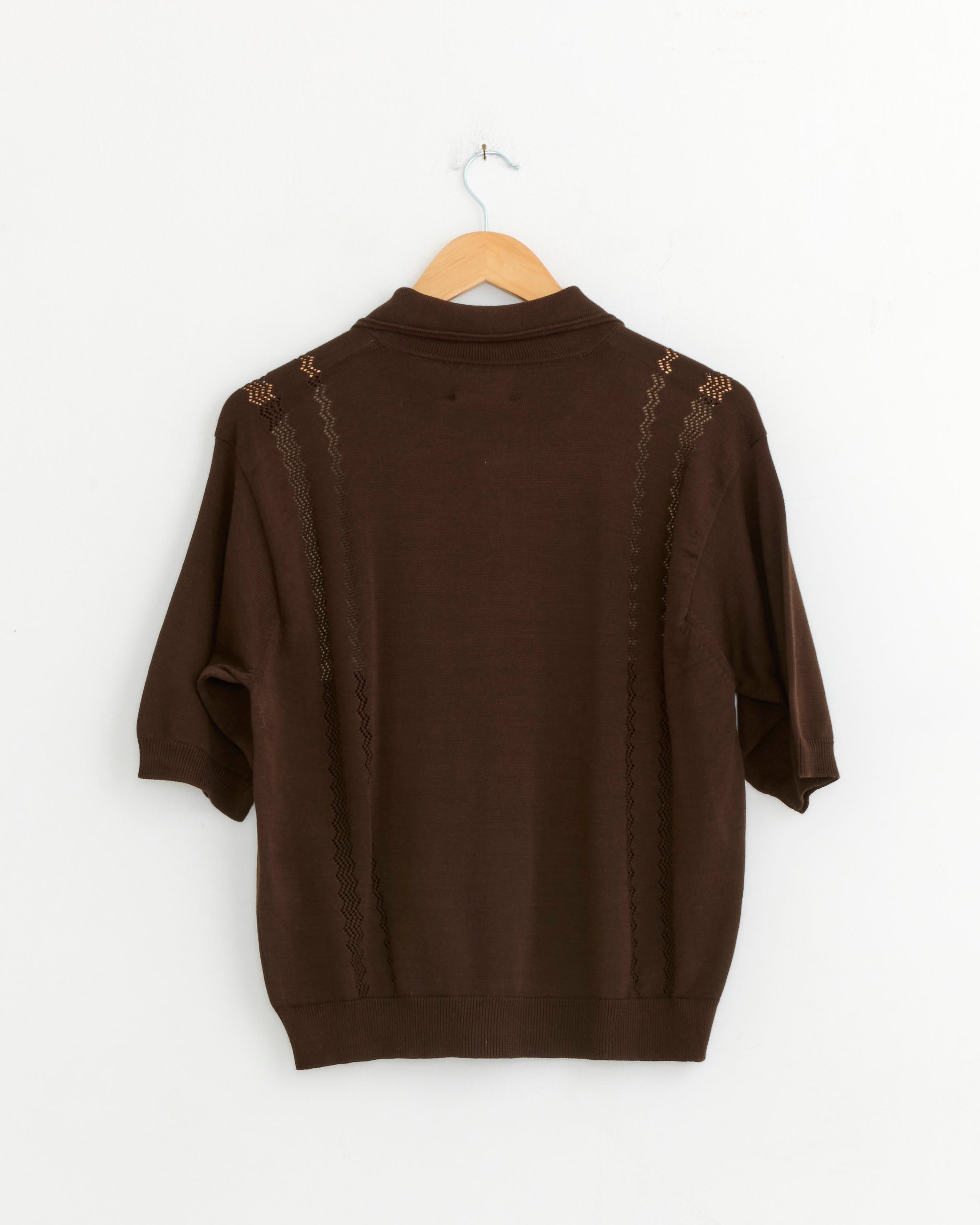 The CORDERA Colorblock Polo in Brown, featuring decorative stitching, hangs on a wooden hanger against a plain white wall, shown from the back.