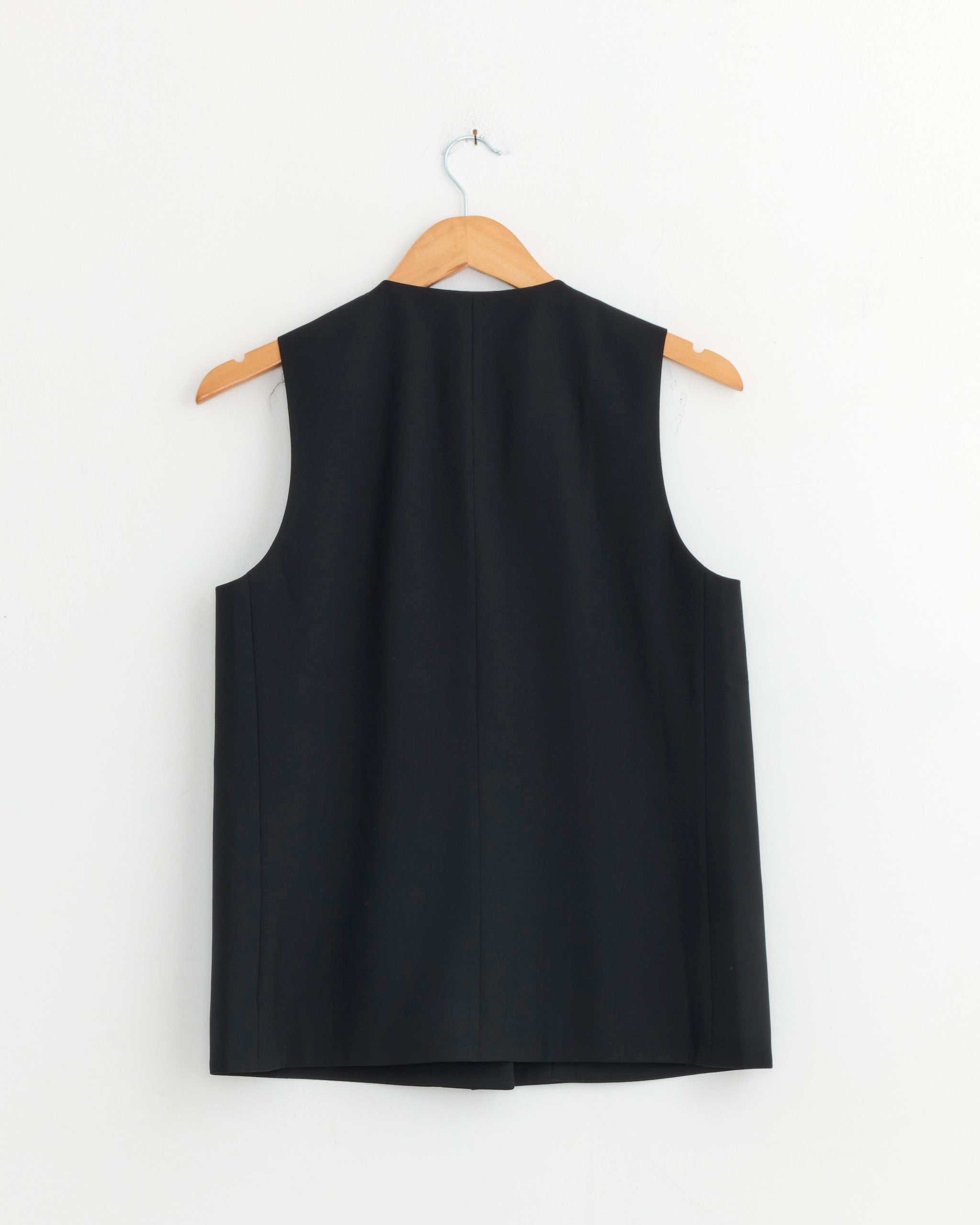 A CORDERA Tailored Vest in Navy hangs sleeveless on a wooden hanger against a plain white wall, shown from the back.