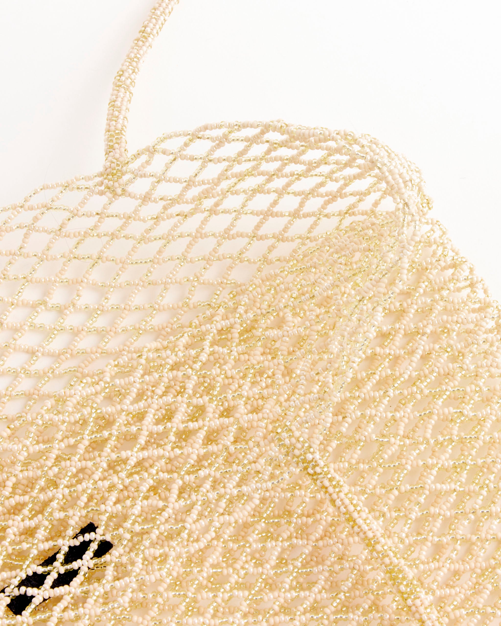 A close-up of the CORDERA Handmade Beaded Tote Bag in Cream shows its netted, open-weave pattern and beaded texture, reflecting exquisite Guatemalan craftsmanship as it rests on a white surface.