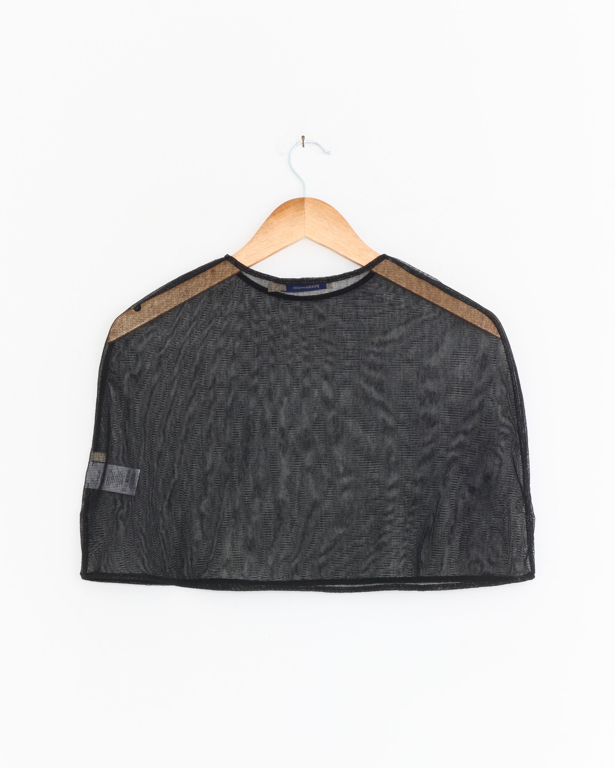 The Boldo Cape in Black by Paloma Wool, a sheer cotton tulle garment, hangs on a wooden hanger against a white background.