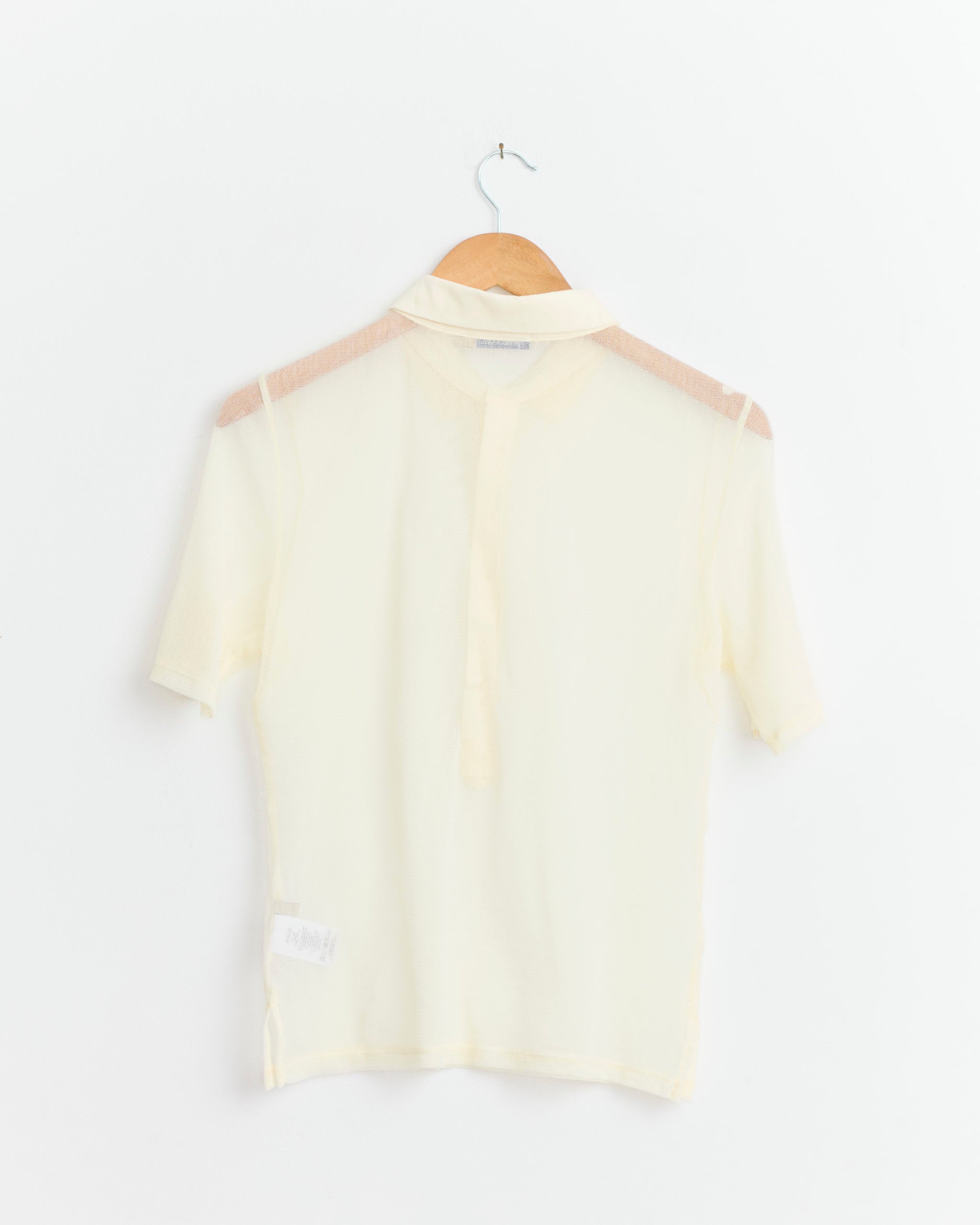 The Paloma Wool Sile Top in Off White is a sheer, lightweight cotton tulle polo-style blouse with short sleeves, collar, and partial button placket, shown on a wooden hanger against a white background.
