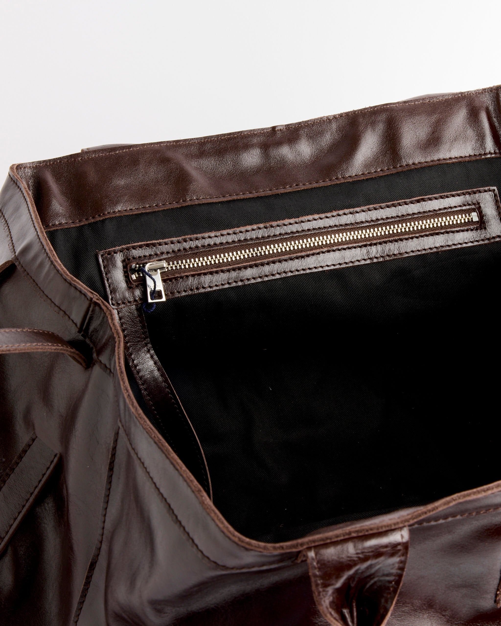The Big Guida Bag in Brown by Paloma Wool features an open 100% leather design with a black fabric interior, a silver zippered pocket stitched inside, and visible edges. The bag is made in España (COO).