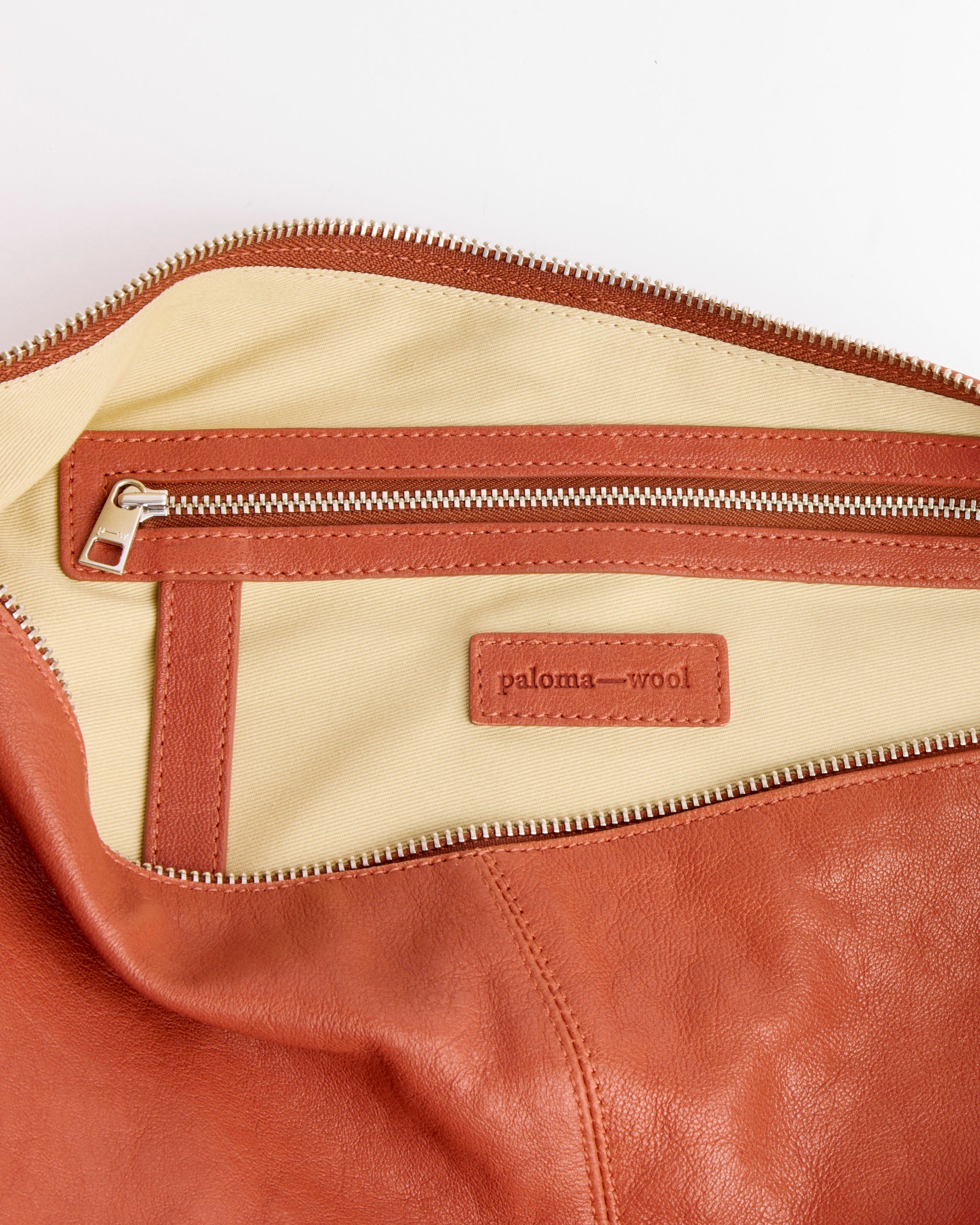 A close-up of the inside of the Paloma Wool Dry Bag in Brown, a leather shoulder bag with beige lining, zippered pocket, and a stitched label reading "paloma—wool".