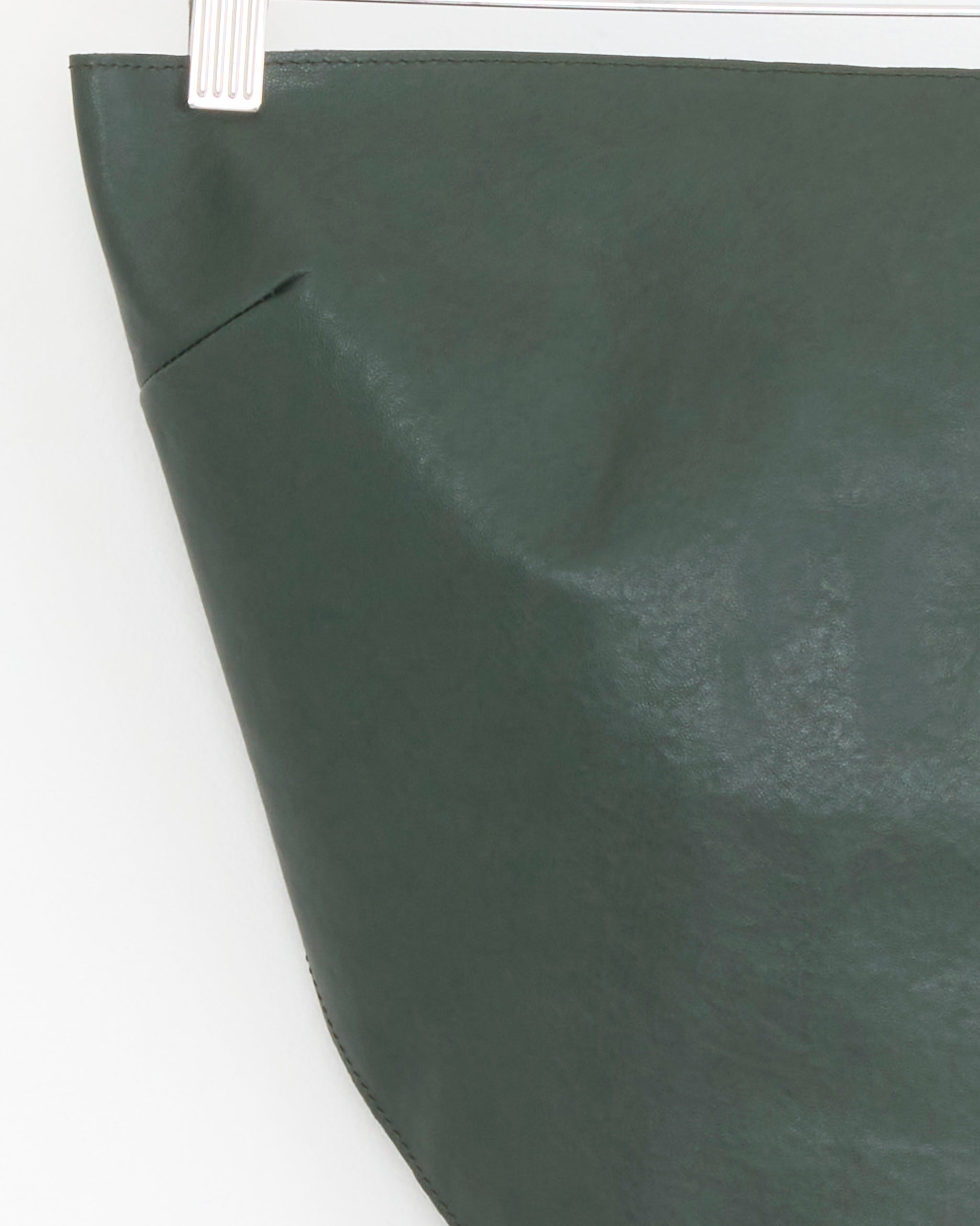 A close-up of the Alba Top in Khaki by Paloma Wool, featuring an asymmetric hemline, shown hanging on a white plastic clip against a white background. Only the upper corner and part of the side seam are visible.