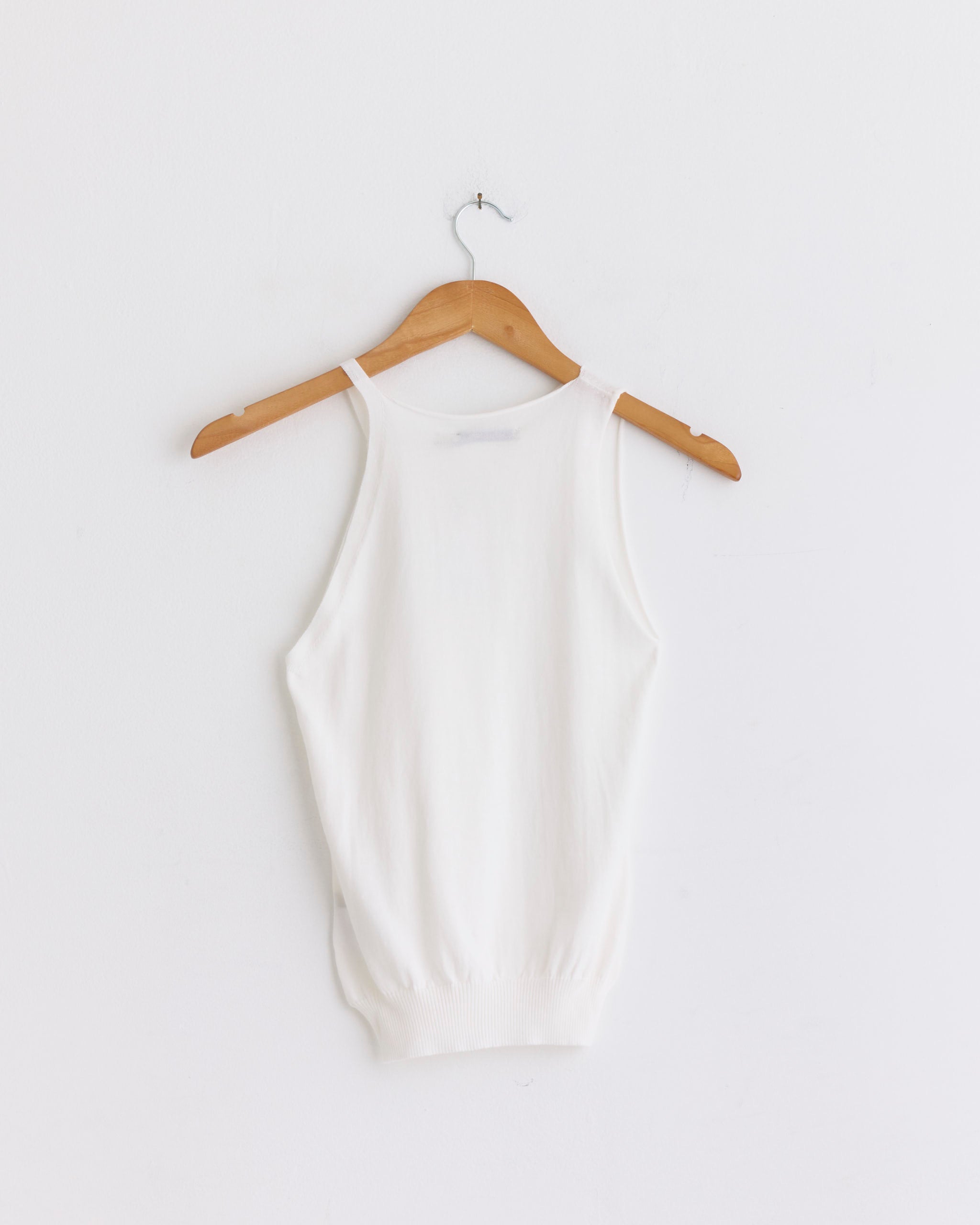 The Lani Tank in Off White by Paloma Wool is a sleeveless knit top made from soft Mako Cotton, shown on a wooden hanger against a plain white wall.