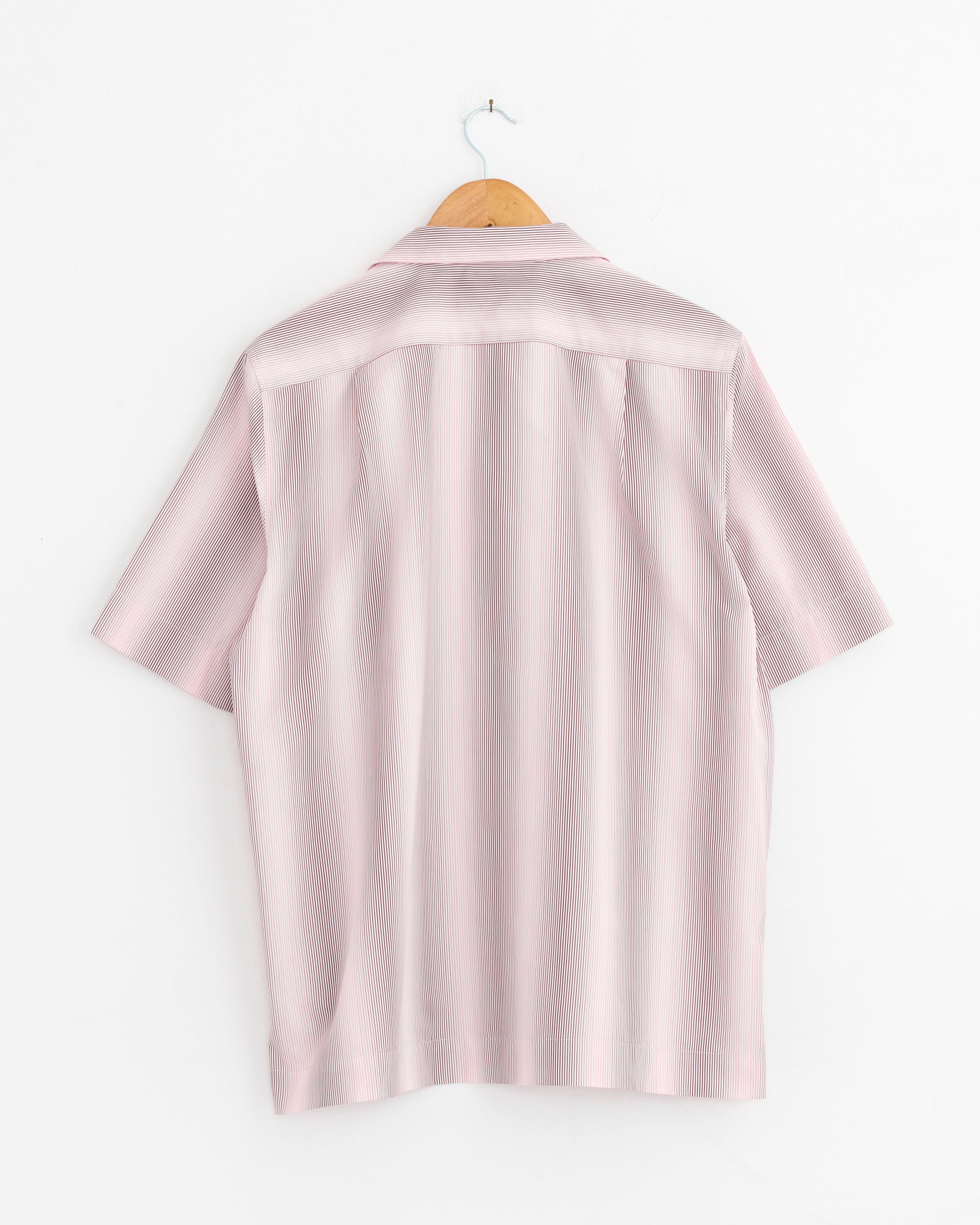 The Dries Van Noten Striped Shirt in Pink, featuring short sleeves and lightweight cotton, is displayed from the back on a wooden hanger against a plain white wall.