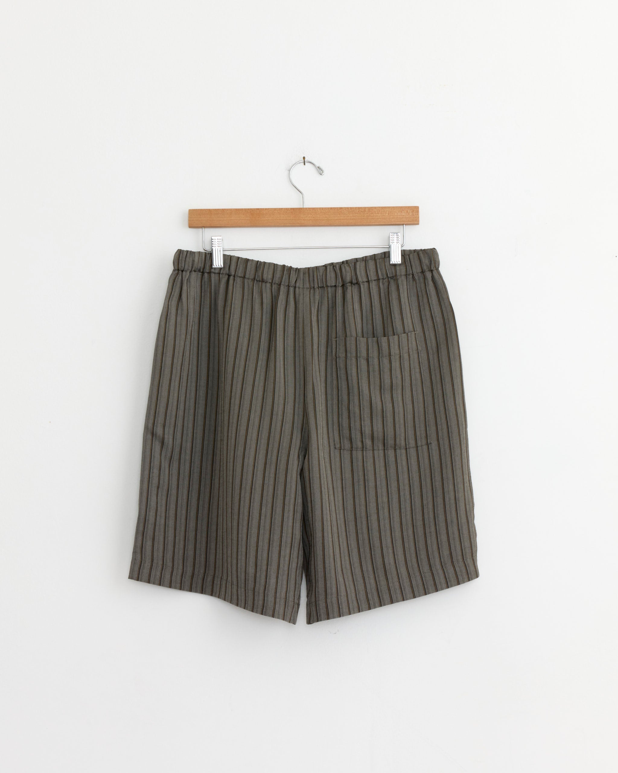 Dries Van Noten Piperi Shorts in Grey, with vertical black stripes, an elastic waistband, and a right patch pocket, hang from a wooden hanger against a white background.