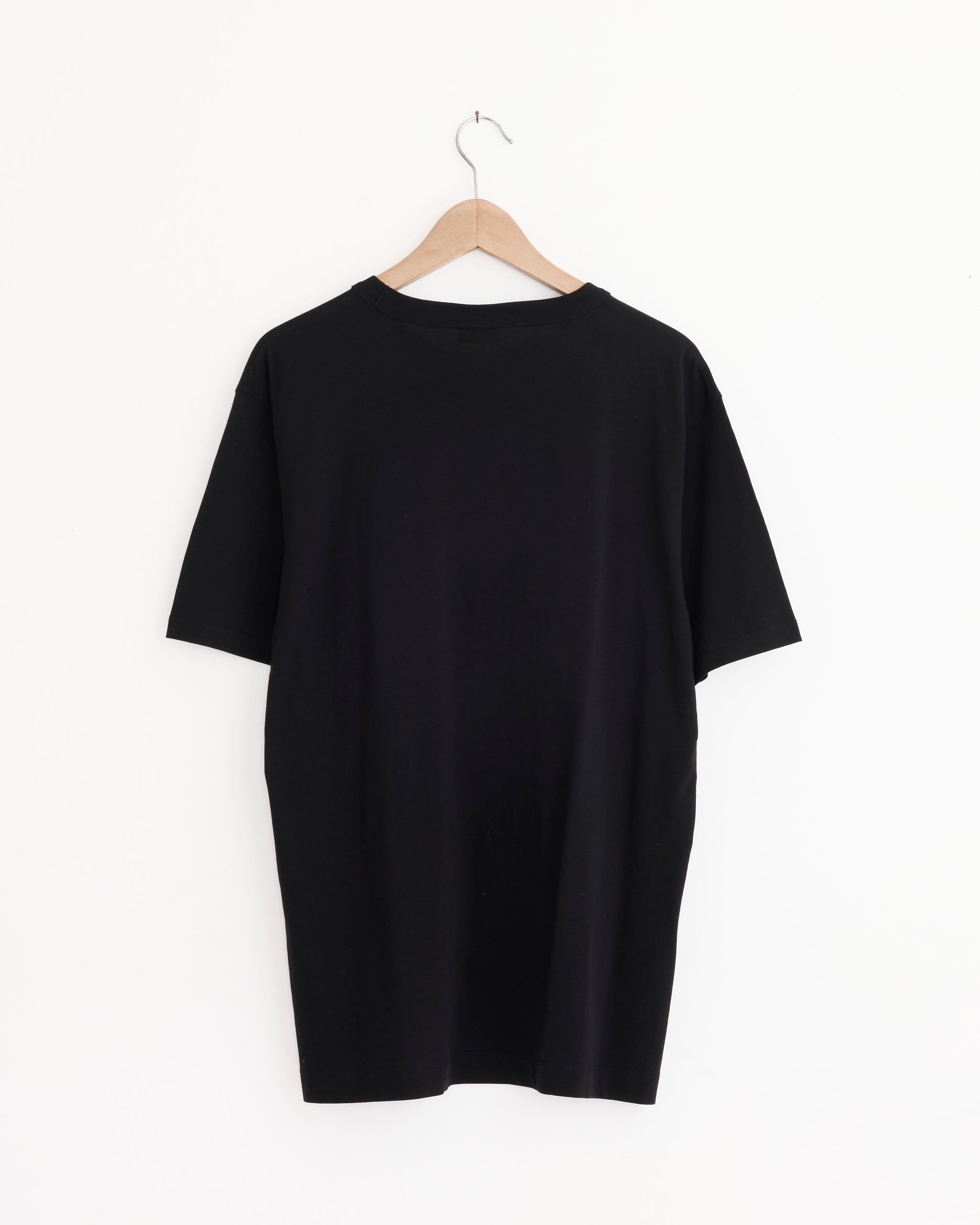 The Dries Van Noten Cotton T-Shirt in Black, made from heavyweight cotton, is shown from the back on a wooden hanger against a white background. It features an oversized crew neck and a simple, classic design.