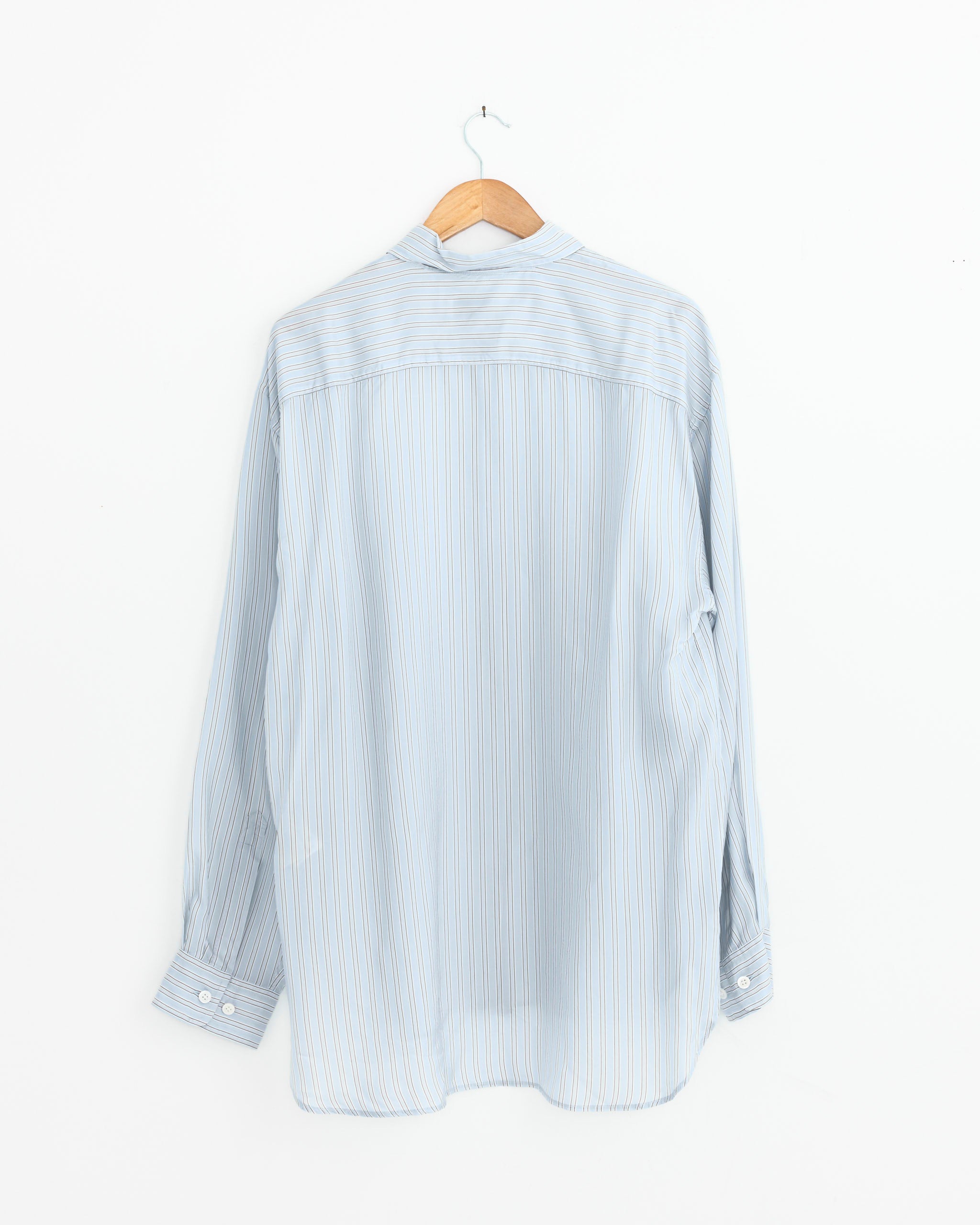 The Striped Shirt in Light Blue by Dries Van Noten, crafted from sustainable fabric with white and yellow vertical stripes, long sleeves, and button-up back view, is displayed on a wooden hanger against a plain white wall.