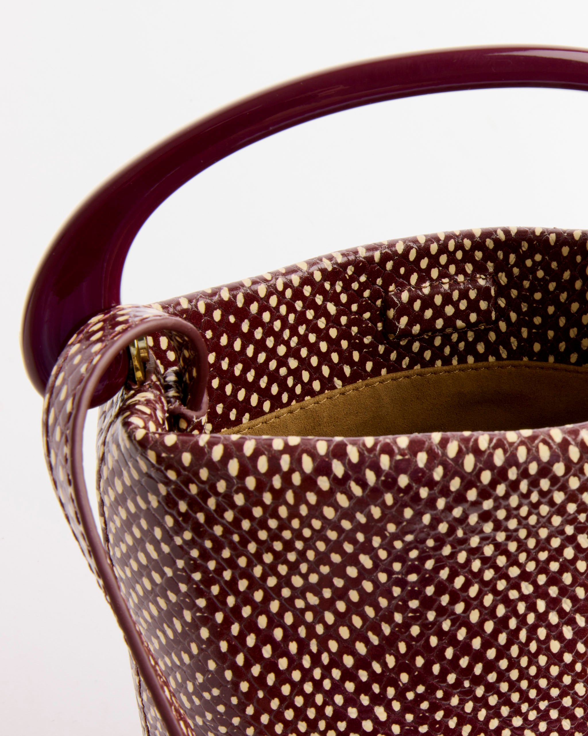 Close-up of the Dries Van Noten Leather Bag in Bordeaux, featuring a curved maroon handle, textured white polka dots, and a snakeskin-embossed finish. The interior is lined in rich brown for an elegant touch.