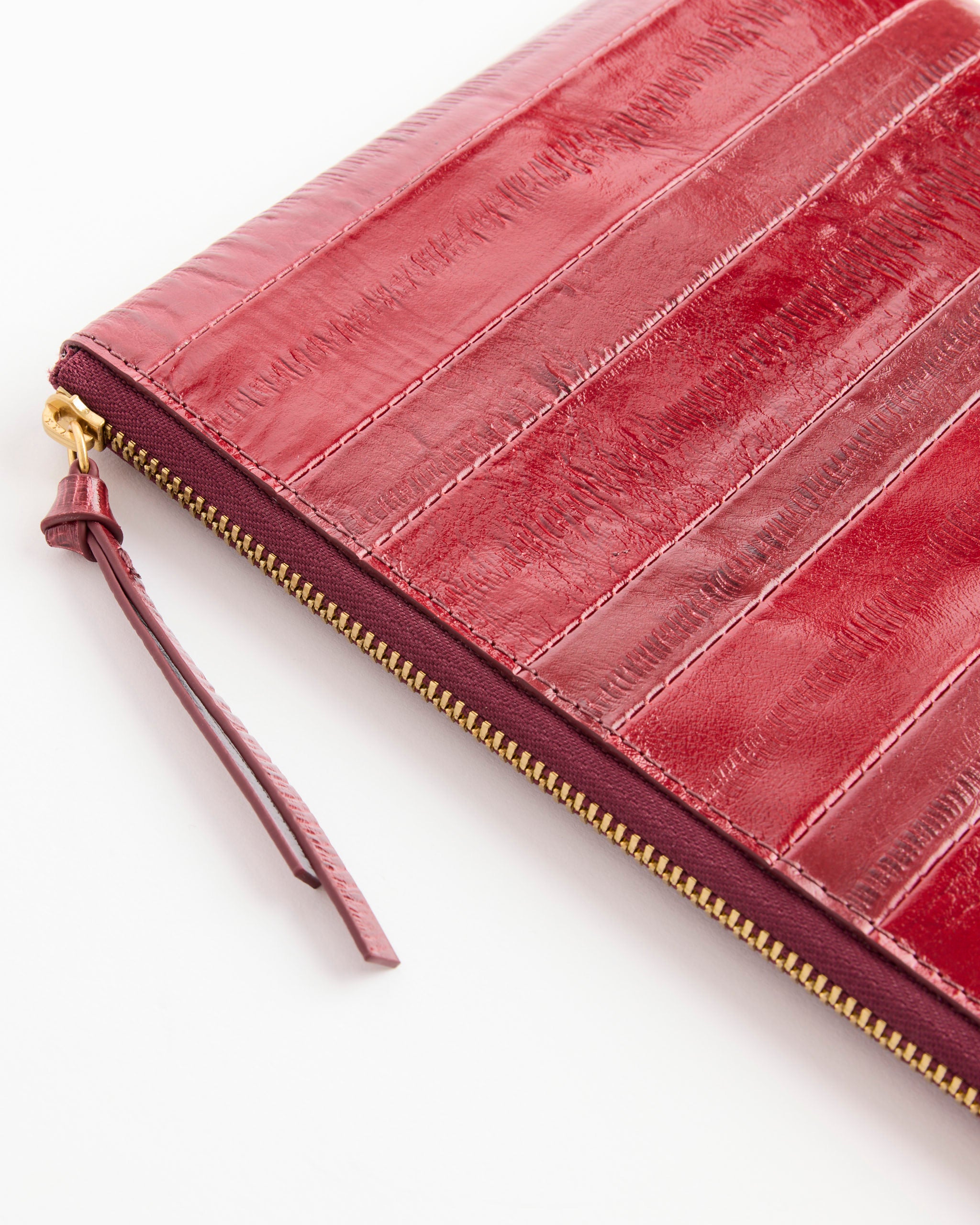 A close-up of the Dries Van Noten Pouch in Red, featuring textured striped calfskin leather and a gold zipper with a leather pull tab, crafted in Italy and set against a white background.