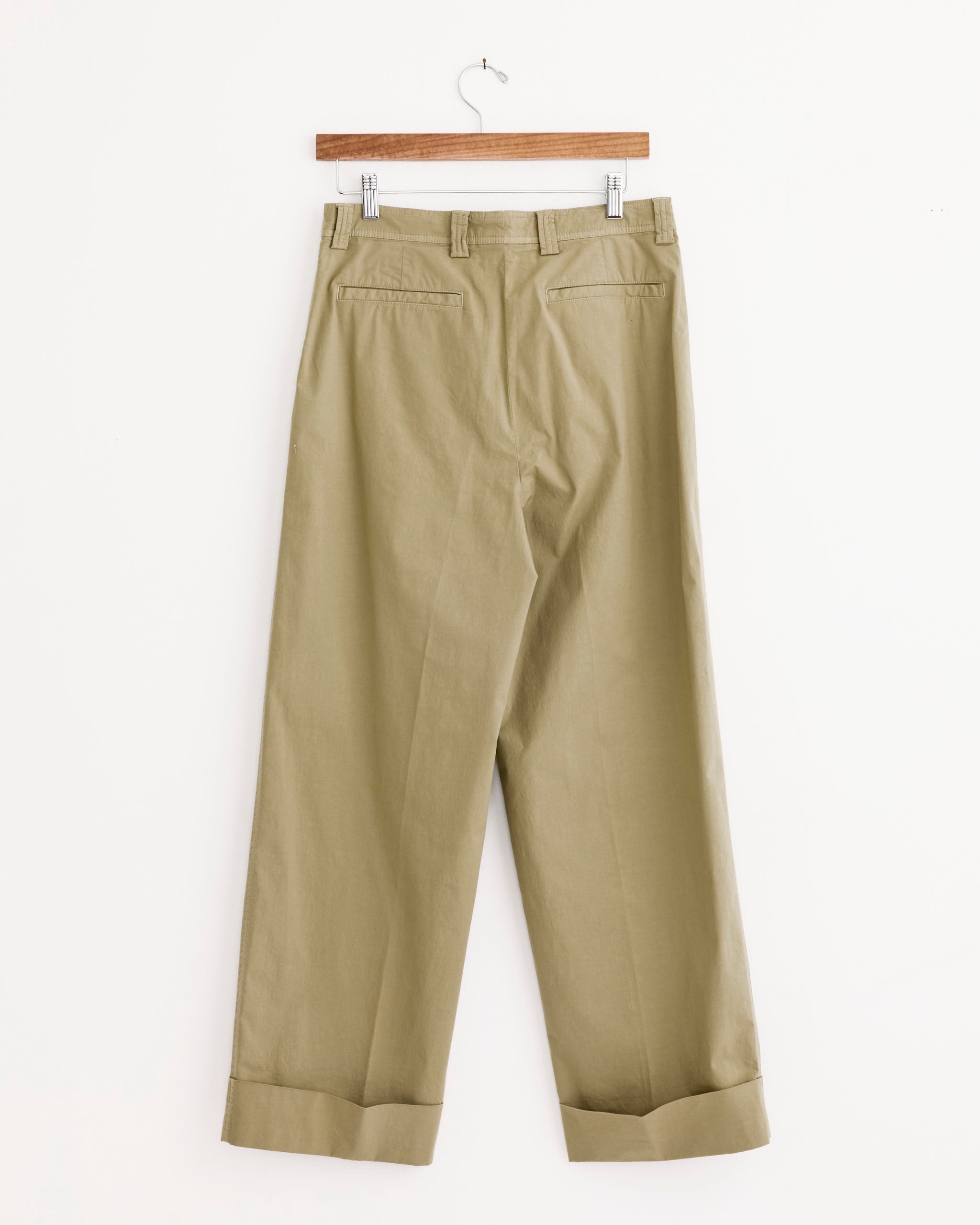 A pair of Dries Van Noten Pakora Bis Pant in Cement, featuring wide legs, cuffs, belt loops, and welt back pockets, hangs on a wooden hanger against a white background.