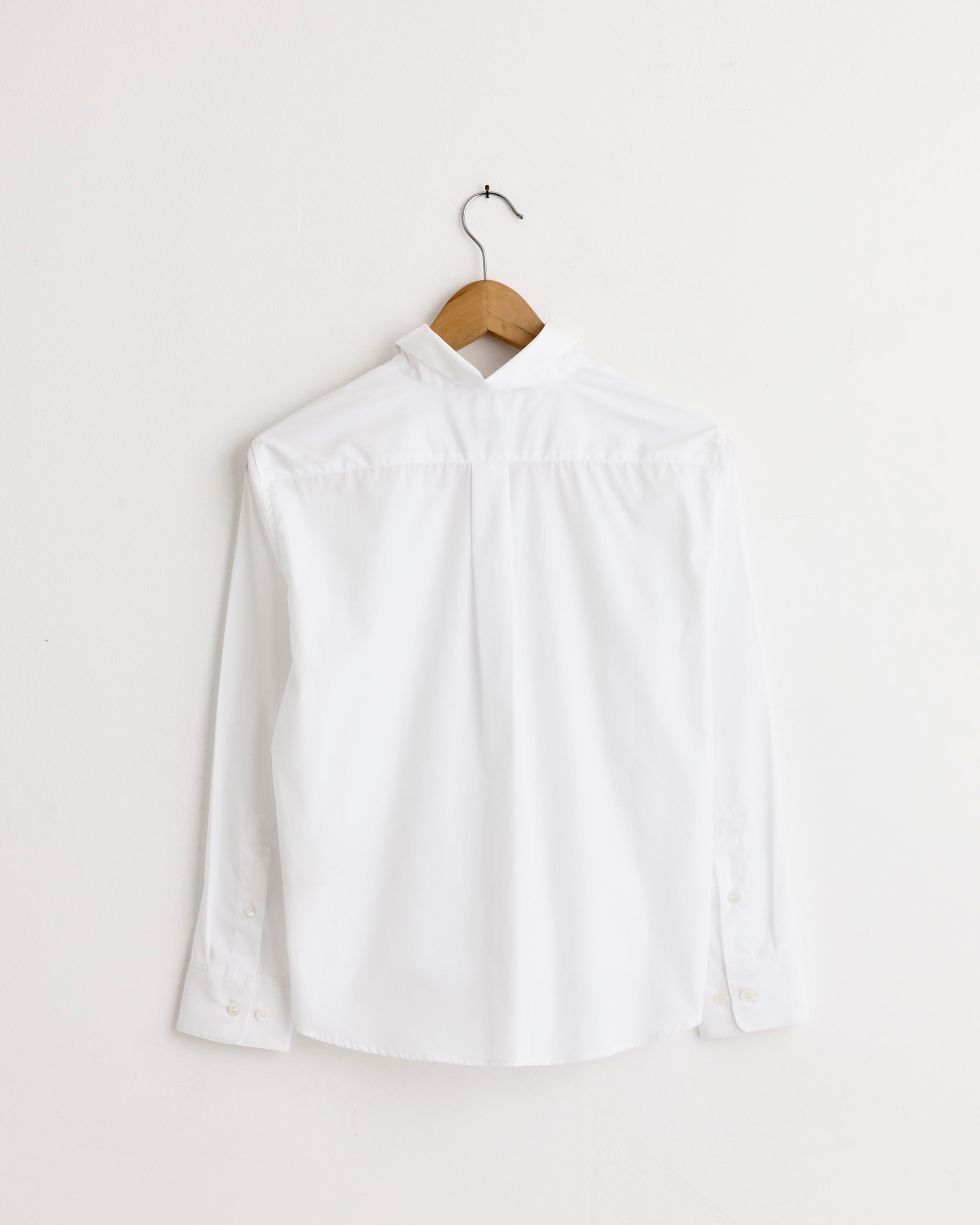 The Dries Van Noten Clavini Bis Shirt in White, made from cotton, is shown from the back on a wooden hanger against a plain white wall.