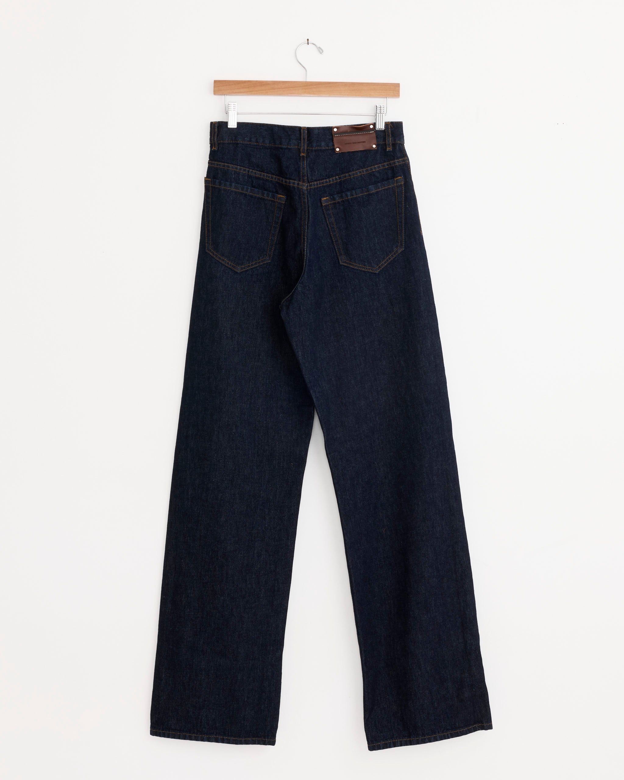 A pair of Dries Van Noten Peyton Denim Pant in Indigo, made from 100% cotton with wide legs and two back pockets with visible stitching, hangs on a wooden hanger against a plain white background.