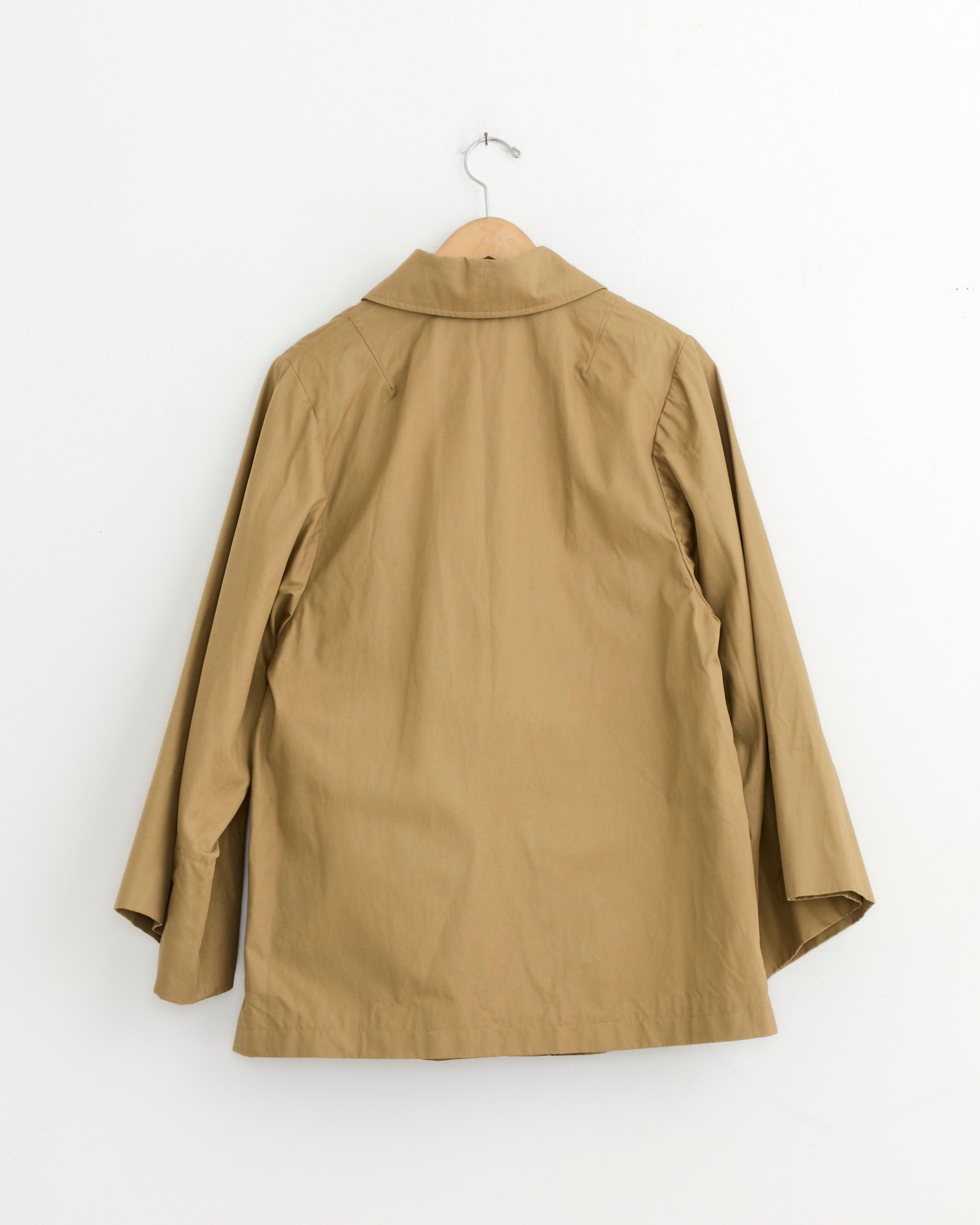 The Dries Van Noten Cotton Coat in Camel, featuring long sleeves and a collar, is displayed from the back on a wooden hanger against a plain white wall.
