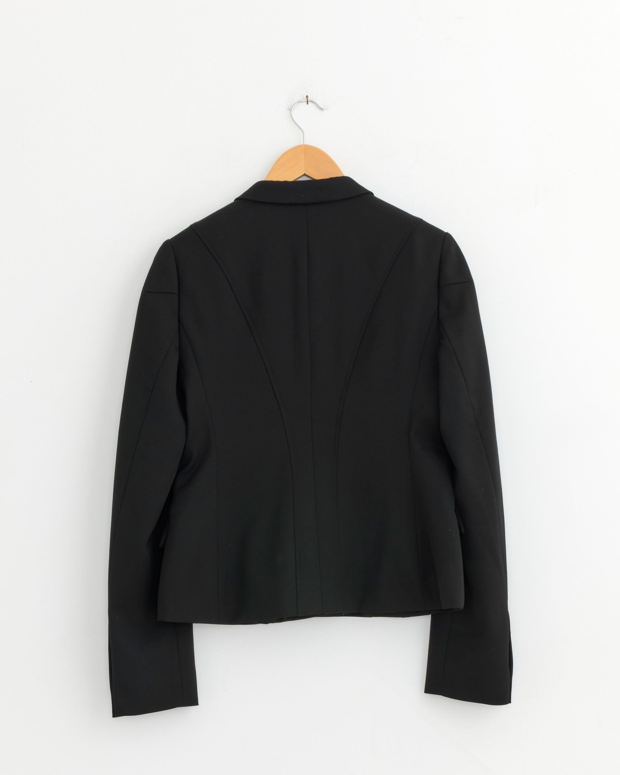 The Dries Van Noten Fitted Jacket in Black is displayed on a wooden hanger against a plain white wall, shown from the back.