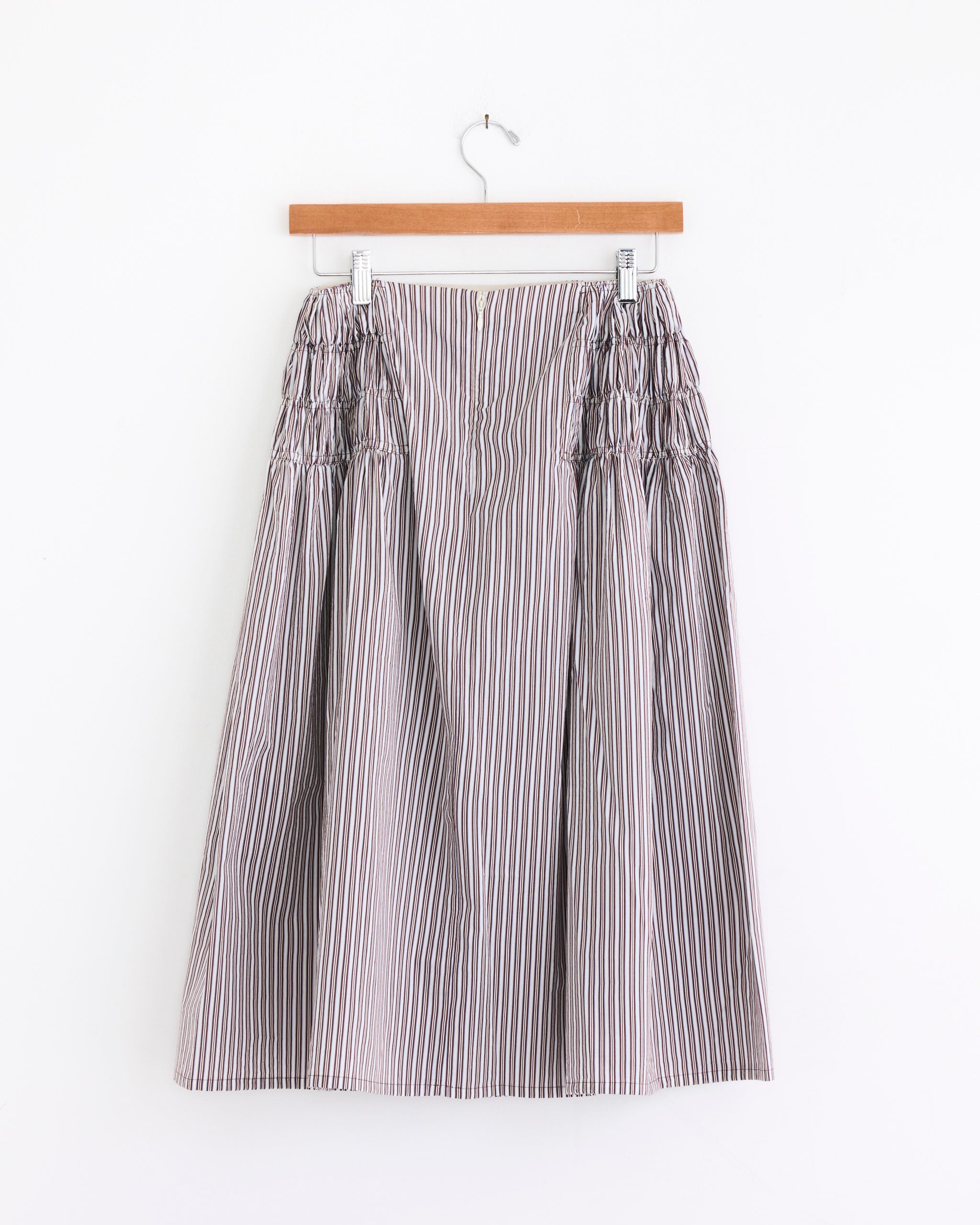 The Dries Van Noten Ruffled Skirt in Brown, crafted from a cotton silk blend with gathered side details, hangs on a wooden hanger against a white background.