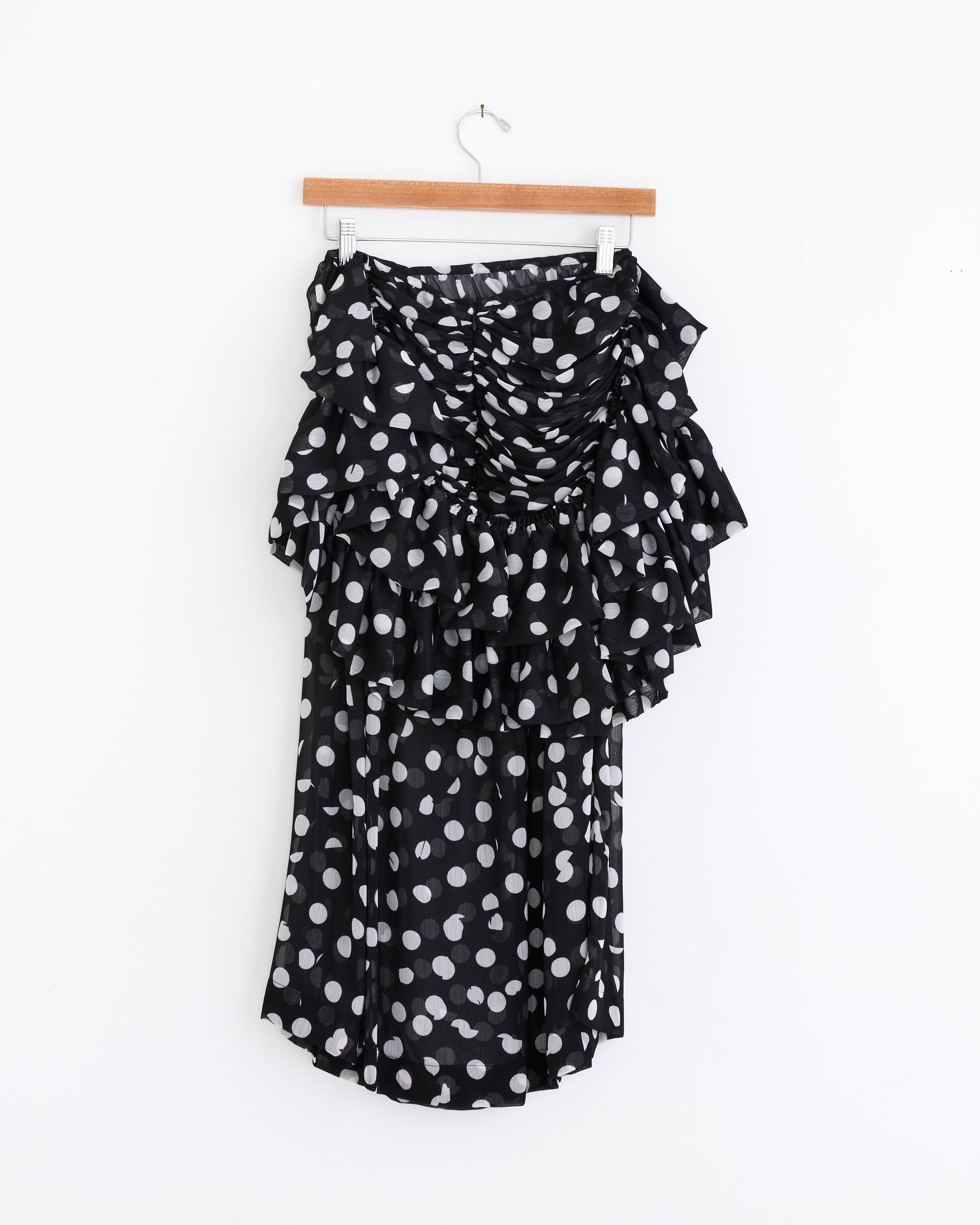 The Dries Van Noten Layered Polka Dot Midi Skirt in Black features ruffled georgette layers and an asymmetric design, shown on a wooden hanger against a plain white background.
