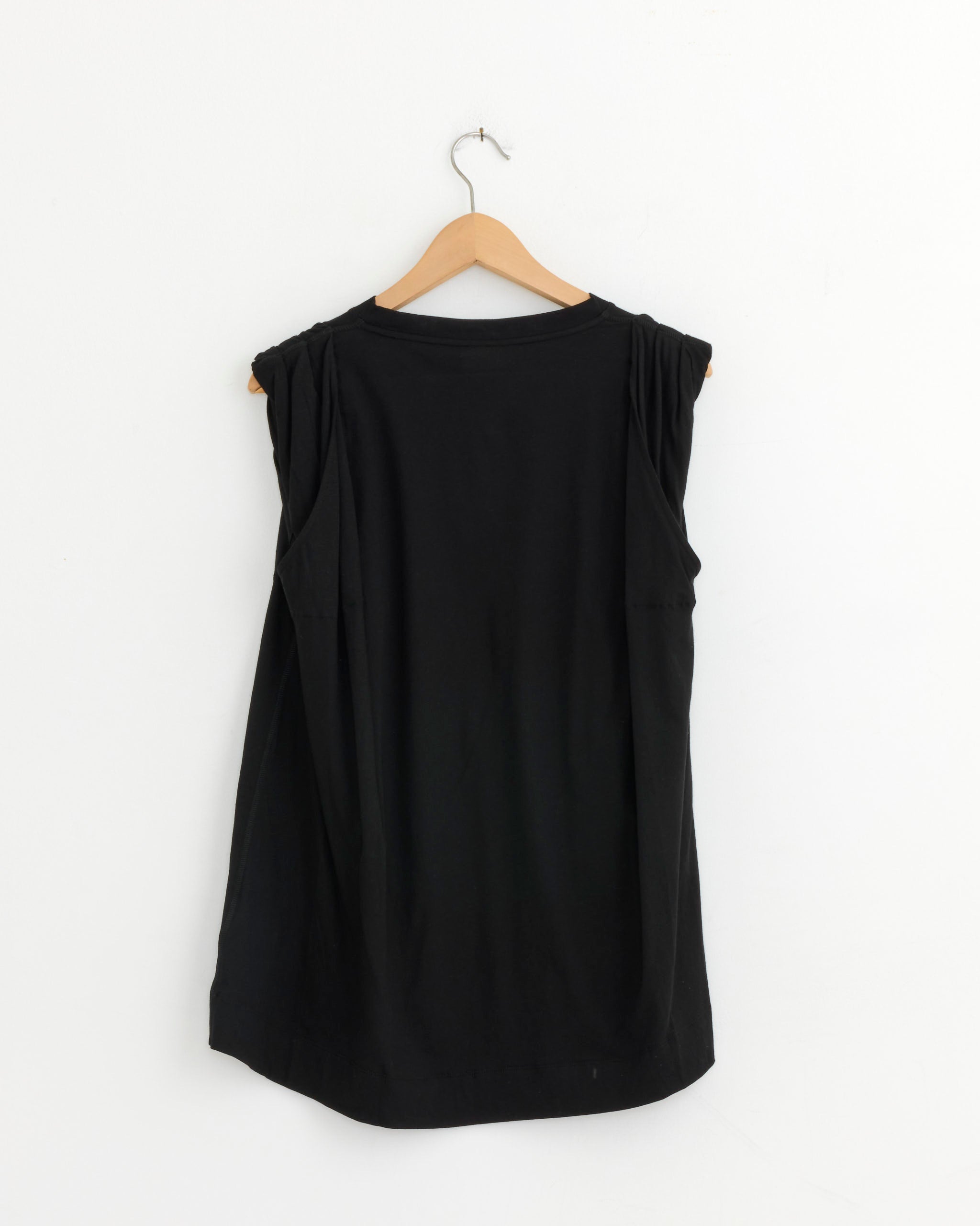 The Dries Van Noten Sleeveless T-Shirt in Black, made of cotton, is displayed from the back on a wooden hanger against a plain white wall.
