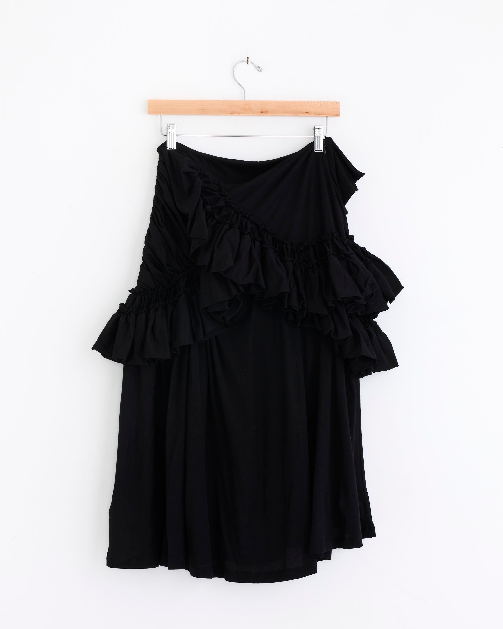 The Dries Van Noten Ruffled Midi Skirt in Black, crafted from cotton jersey with elegant ruffle details and a knee-length cut, is displayed on a wooden hanger against a plain white background.