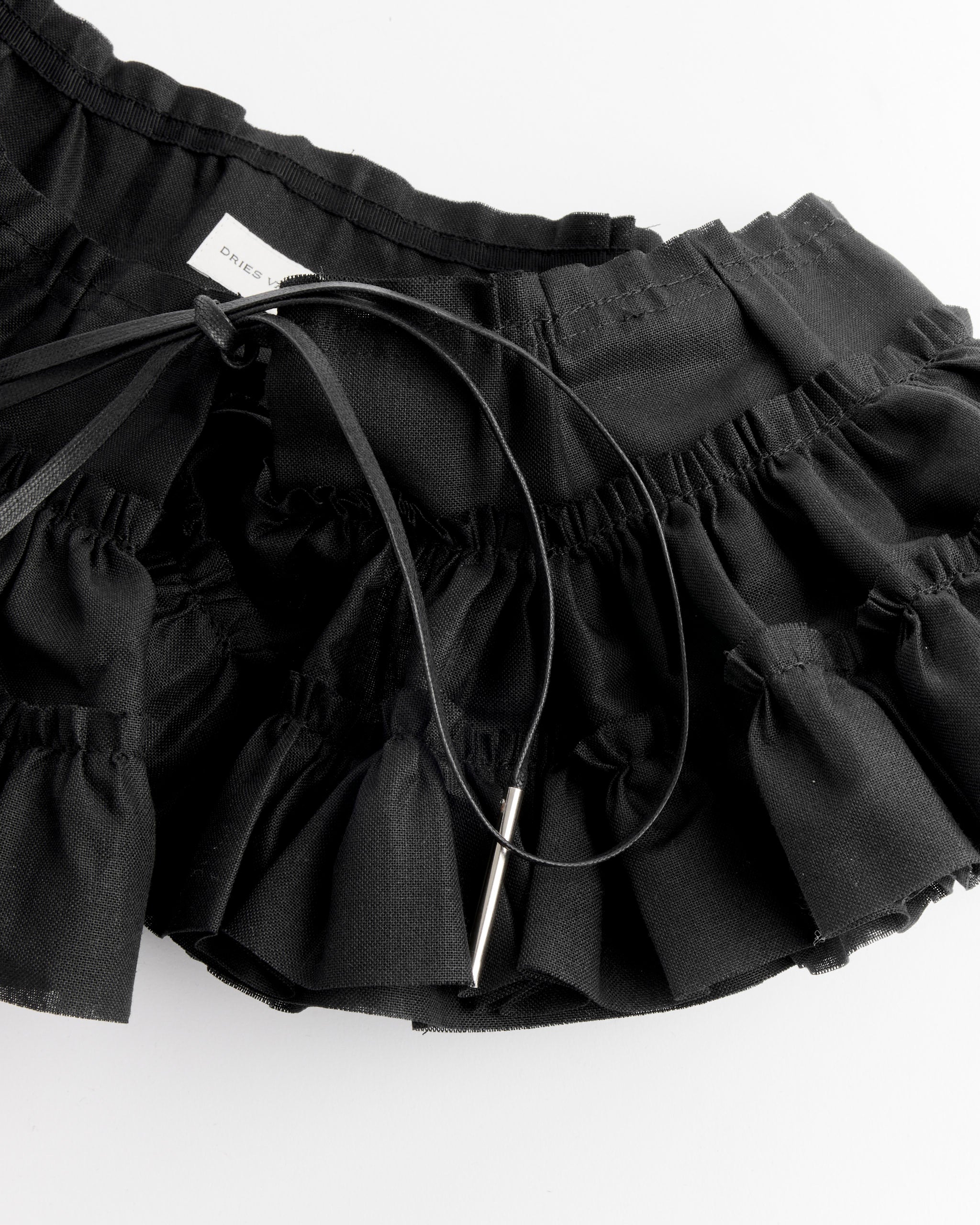 A close-up of the Dries Van Noten Ruffle Belt in Black, featuring ruffled fabric, a drawstring with metal tips, a visible white label, and a ruffle waist belt detail.