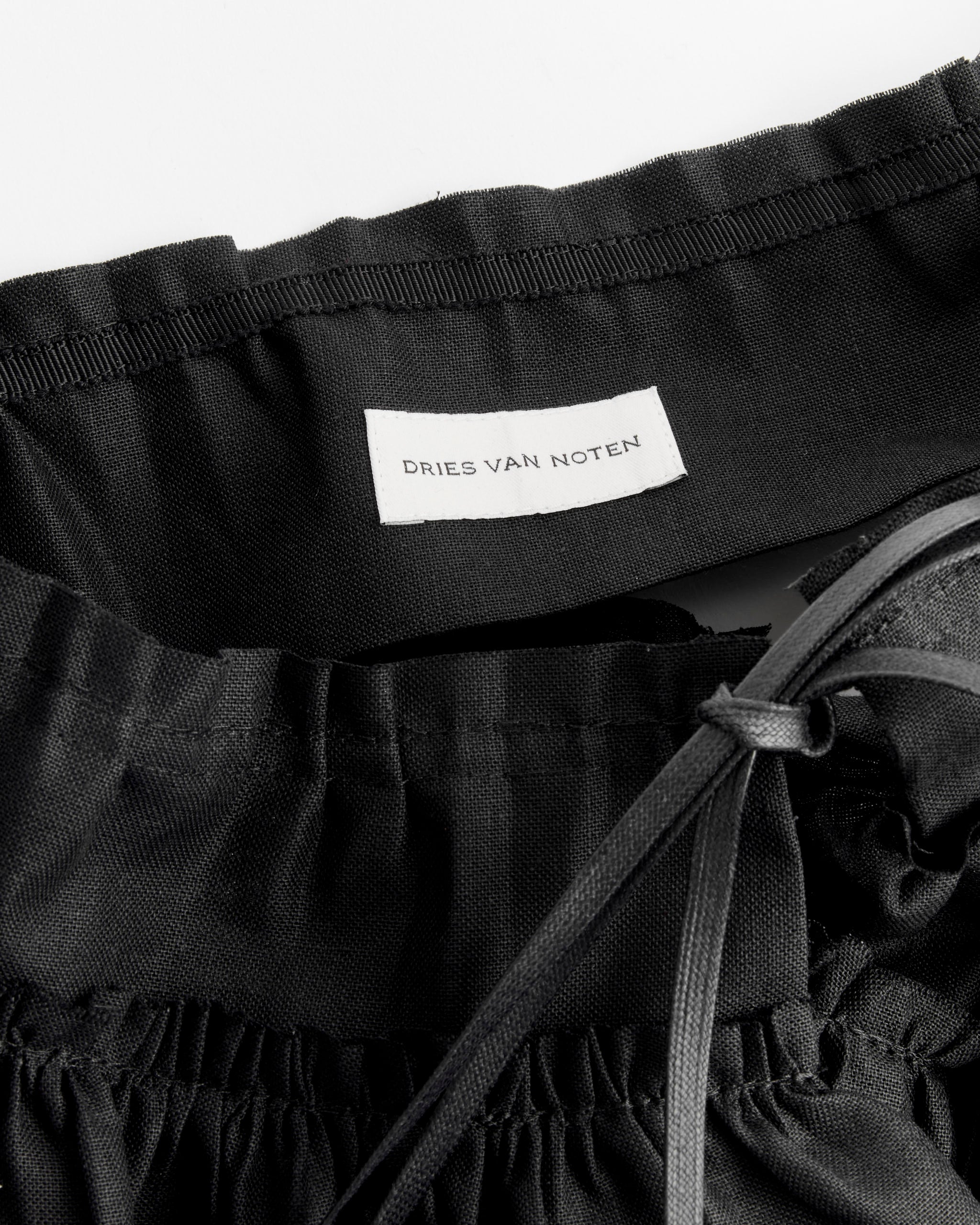 Close-up of black pants with a Dries Van Noten Ruffle Belt in Black, featuring an elastic waistband, drawstring, and an inner white Dries Van Noten label.
