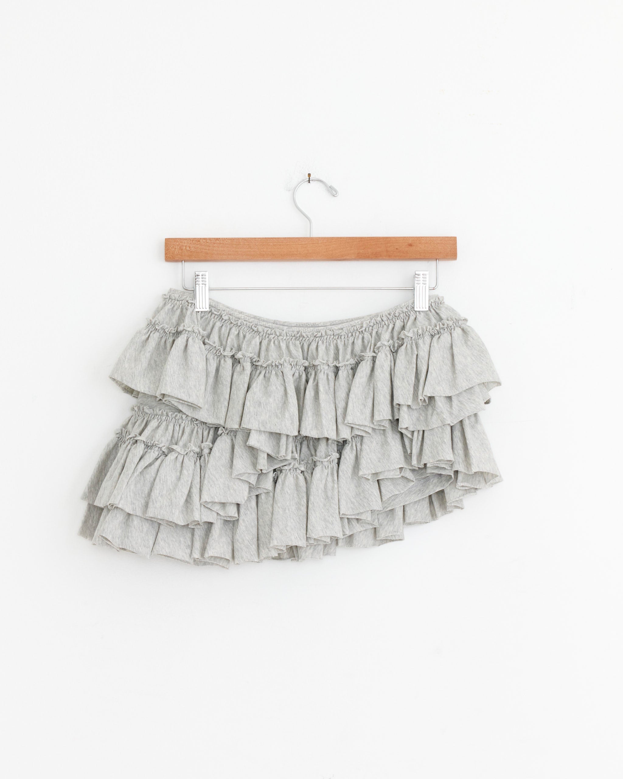 A Dries Van Noten Pleated Jersey Short in Grey Melange hangs on a wooden hanger against a plain white wall.