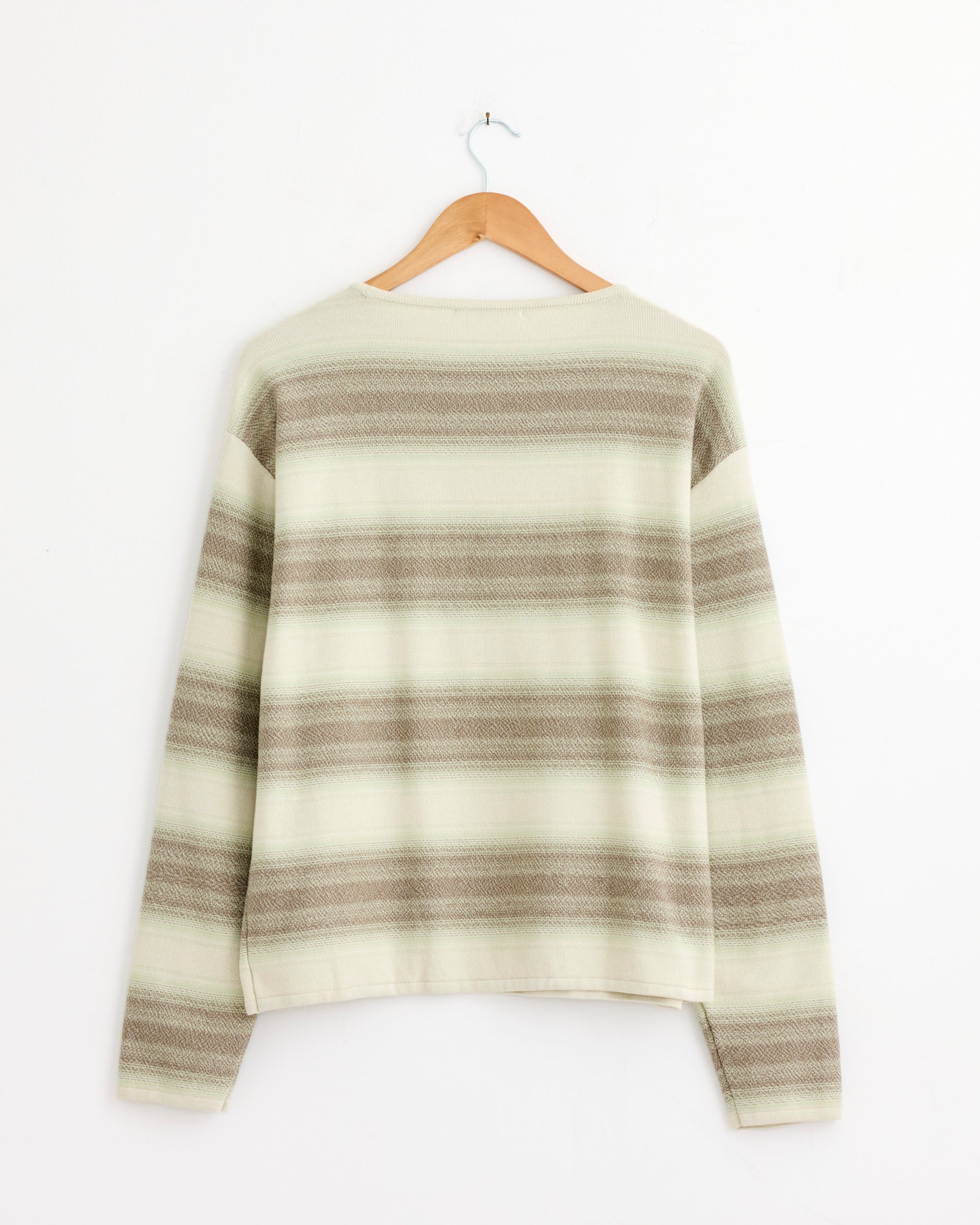 The Auralee Cotton Silk Gradient Stripe Pullover in Lime Grey, featuring long sleeves, is shown from the back on a wooden hanger against a white wall. Expertly crafted in Japan.