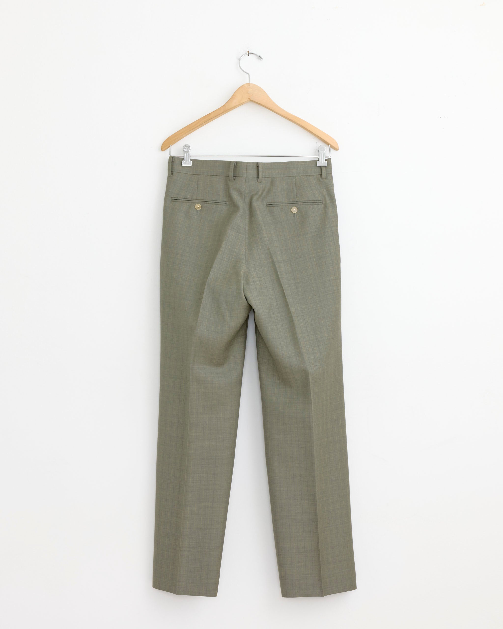The Auralee Bluefaced Wool Stripe Two Tuck Slack in Khaki Grey hangs on a wooden hanger against a white wall, showing the back with two buttoned pockets.
