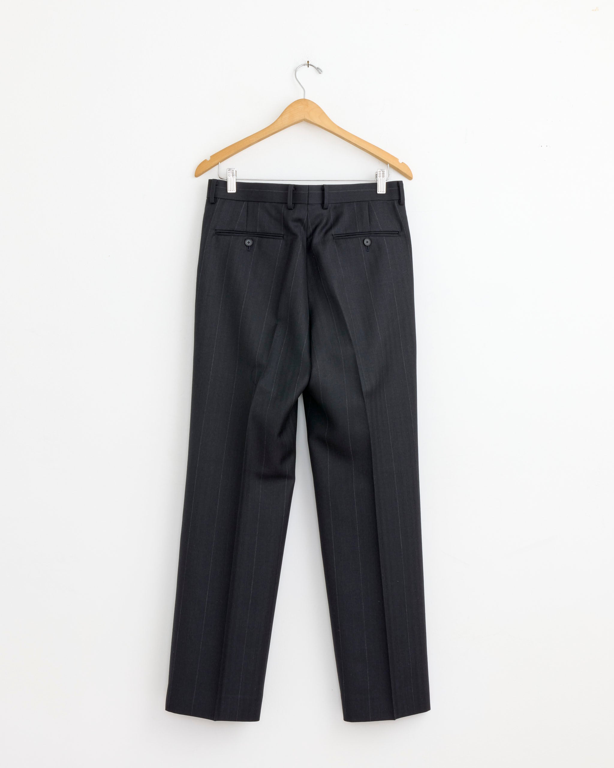 A pair of Auralee Bluefaced Wool Stripe Two Tuck Slack in Charcoal Navy hangs on a wooden hanger against a white background, viewed from the back.