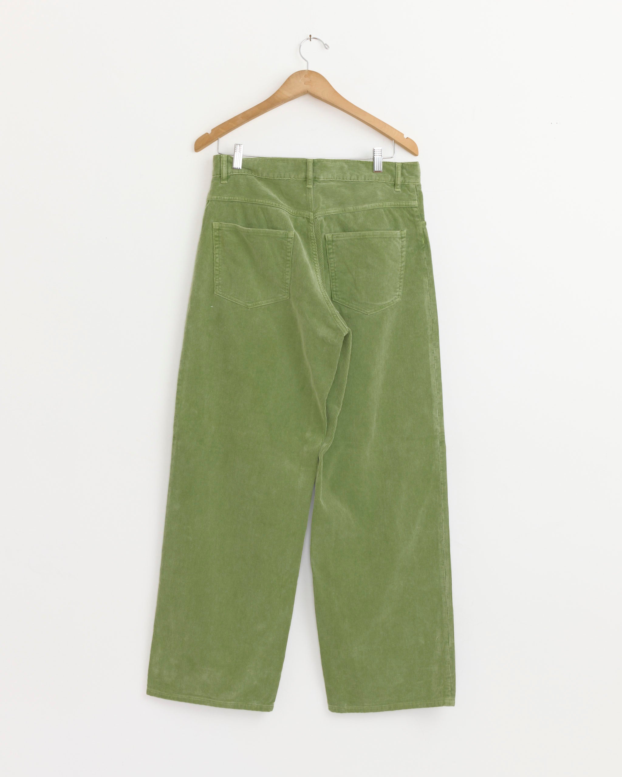 The Auralee Garment Dyed Corduroy 5 Pocket Pant in Dusty Green hangs on a wooden hanger, showing its back pockets, against a plain white background.