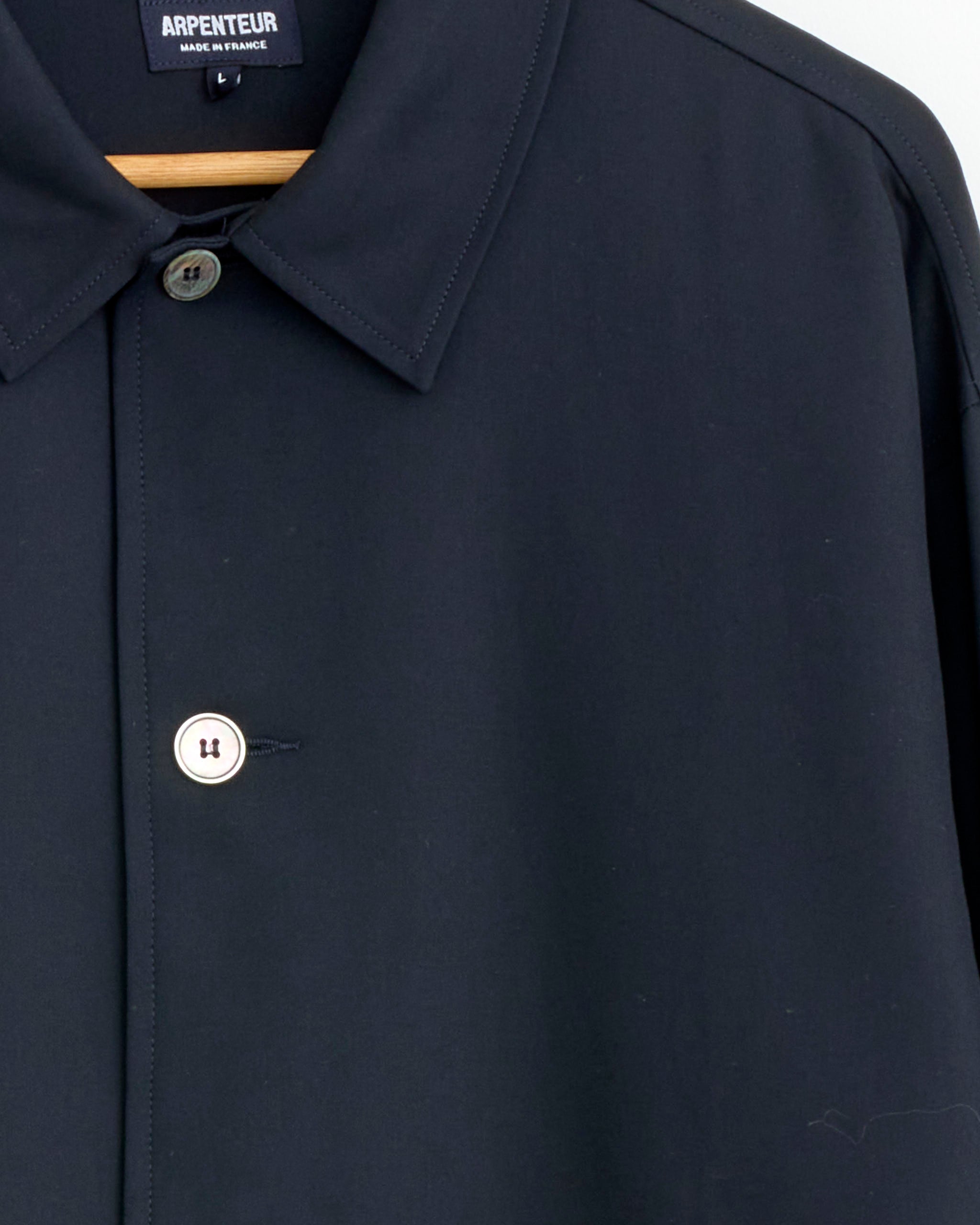 Close-up of the Arpenteur Repos Jacket in Midnight on a hanger, featuring two buttons and part of the inside collar label. The smooth, matte fabric highlights its Made in France quality.