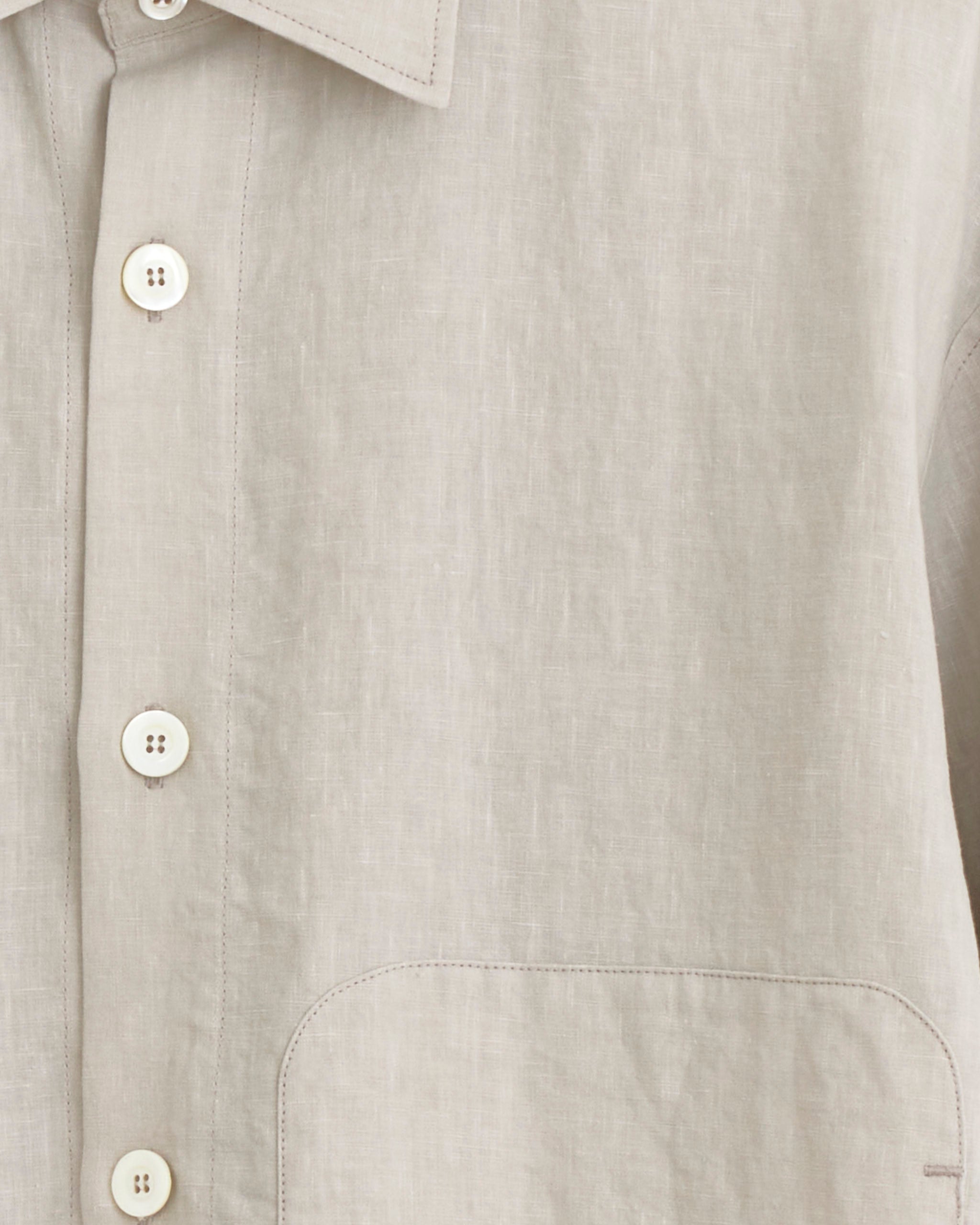 Close-up of the Arpenteur Sigma Jacket in greige, featuring white buttons, part of a collar, a chest pocket, and visible stitching on the soft 100% linen fabric inspired by classic French workwear.