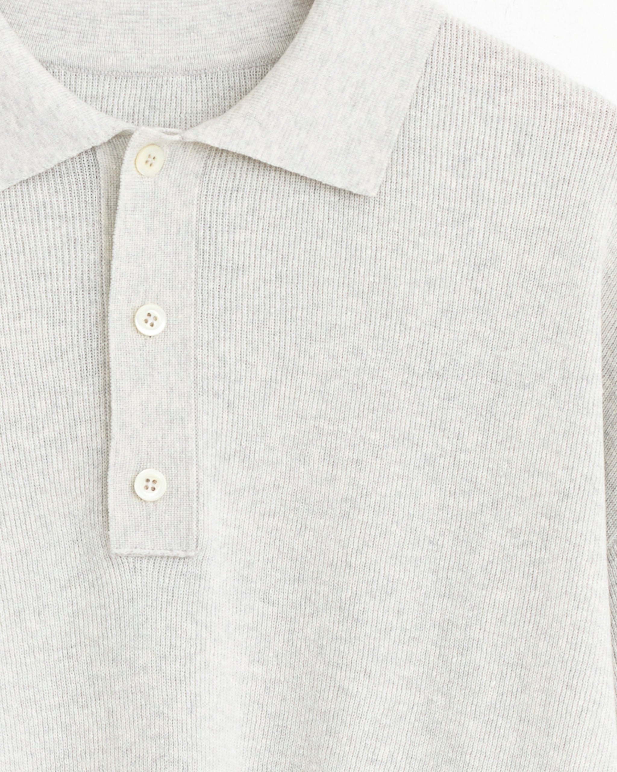 A close-up of the Mile Knit in Pale Grey by Arpenteur, a light grey ribbed polo shirt crafted from a soft linen-cotton blend, featuring a collar and a three-button partial placket with cream-colored buttons.